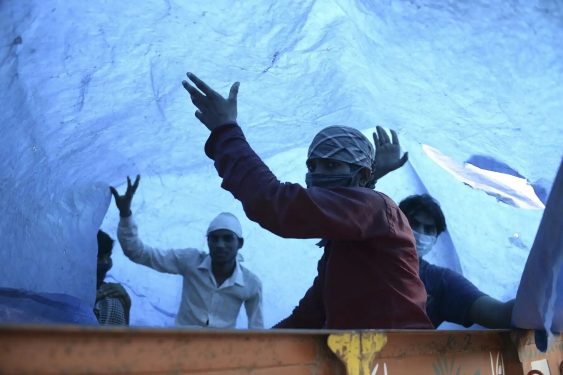Los trabajadores migrantes sostienen una lámina de plástico para proteger la lluvia dentro de un camión cuando regresan a sus ciudades de origen, en las afueras de Hyderabad. Foto: AFP
