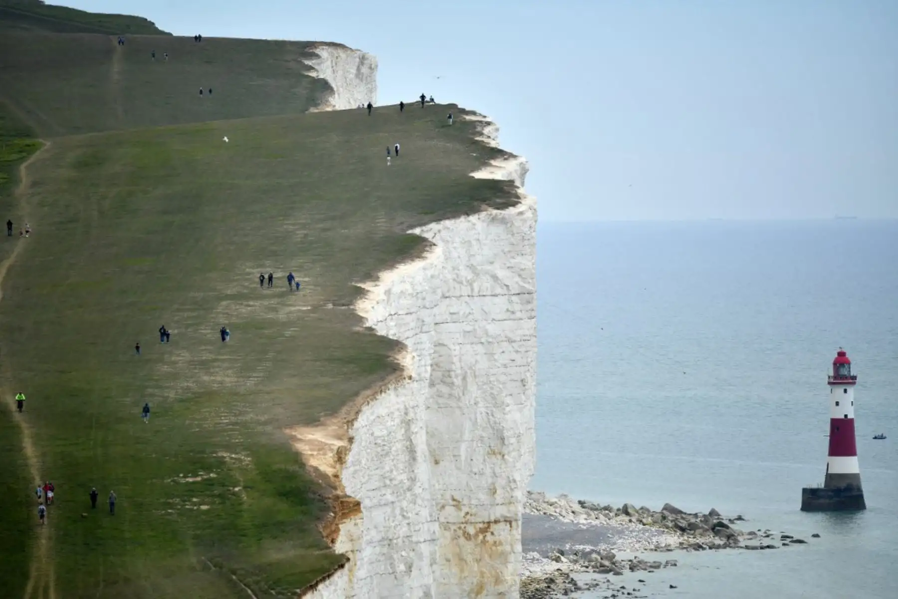 La gente camina por el acantilado sobre el faro en Beachy Head, cerca de Eastbourne, en la costa sur de Inglaterra, después de una flexibilización de las reglas de bloqueo en Inglaterra durante la nueva pandemia de coronavirus. Foto: AFP