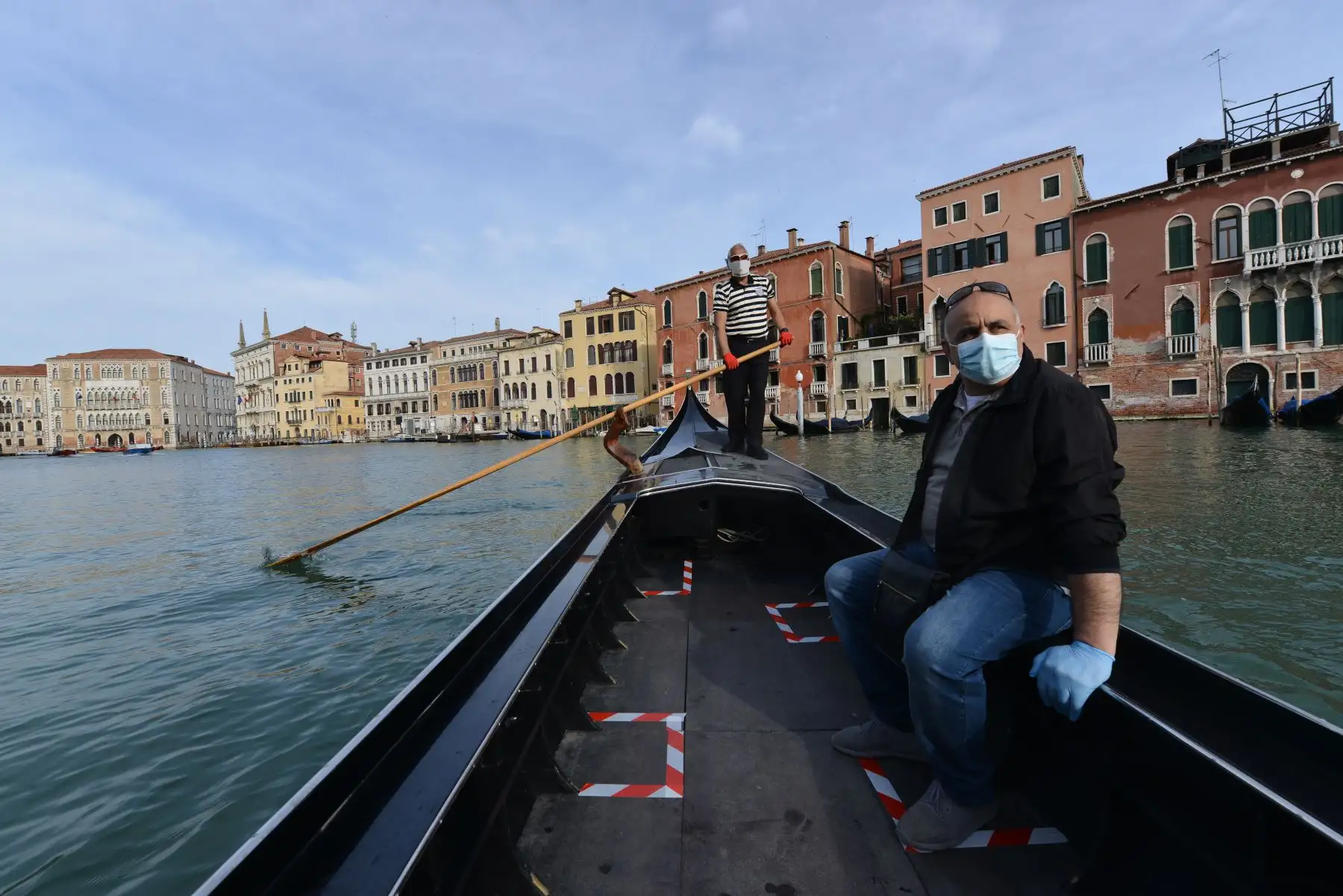 Un gondolero con una máscara facial (trasera) transporta a su primer cliente cuando el servicio se reanuda en el terraplén de San Toma en un canal de Venecia. Foto: AFP
