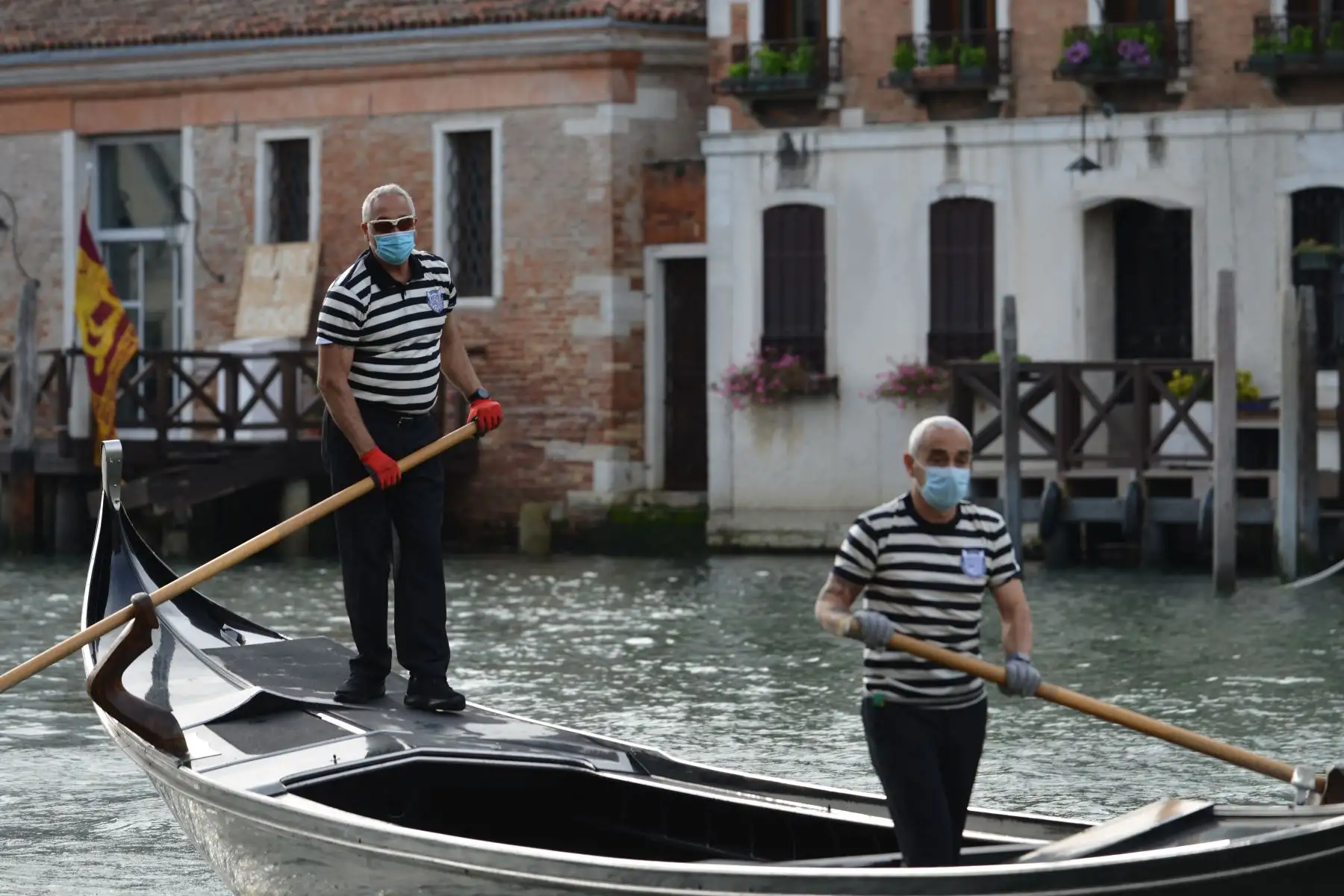 Los gondoleros que llevan una máscara facial suben a una góndola por el terraplén de San Toma en un canal de Venecia mientras reanudan el servicio. Foto: AFP