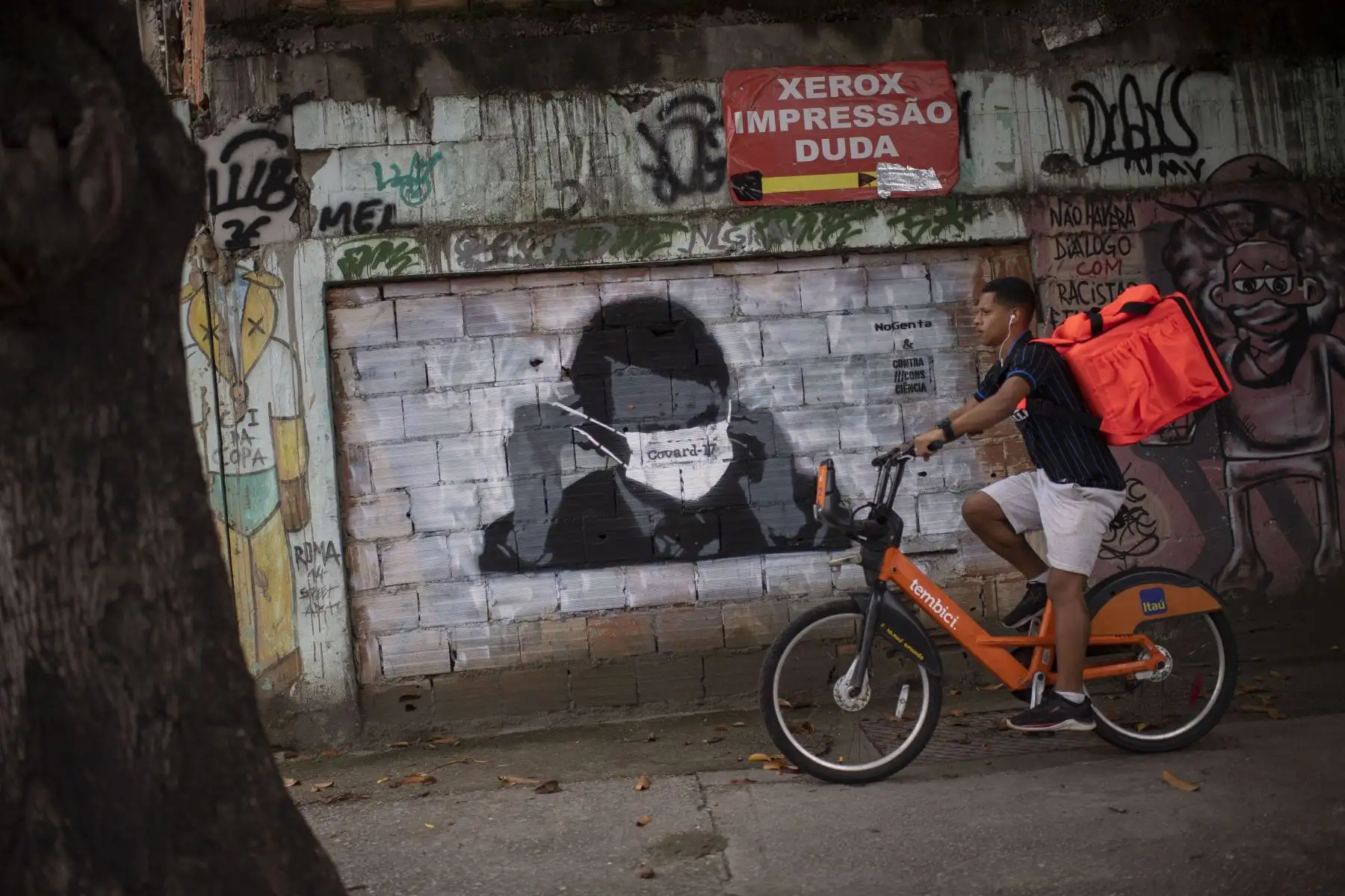 Un graffiti del presidente brasileño Jair Bolsonaro con una máscara facial se ve en una pared mientras un repartidor monta una bicicleta en el centro de Río de Janeiro, Brasil. Foto: AFP