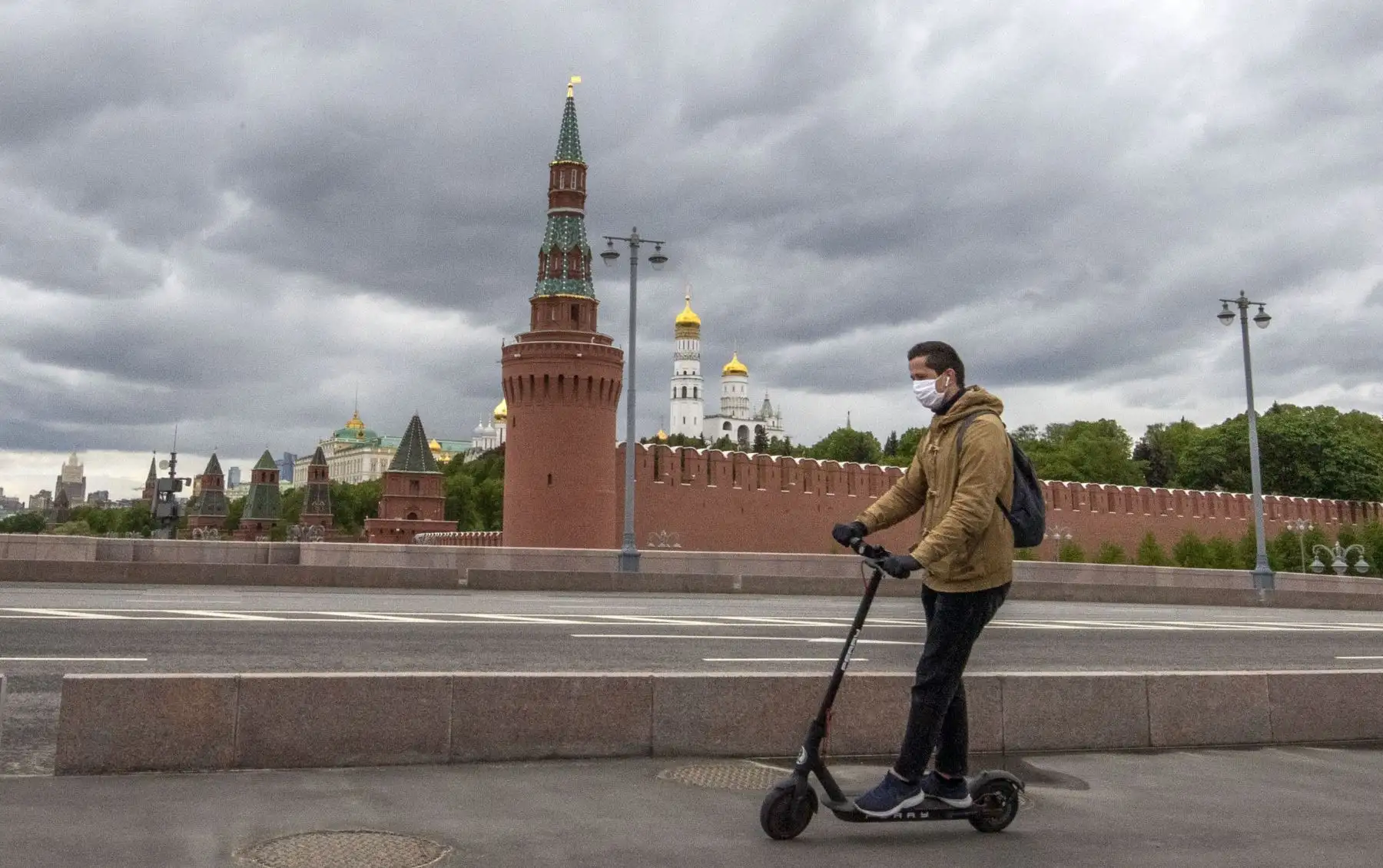 Un hombre con una máscara facial monta un scooter cerca del Kremlin en el centro de Moscú. Foto: AFP