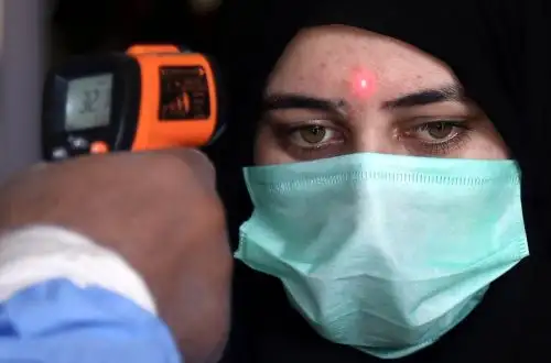Un trabajador de una estación de tren mide la temperatura de una pasajera en Karachi, Pakistán. Foto: EFE
