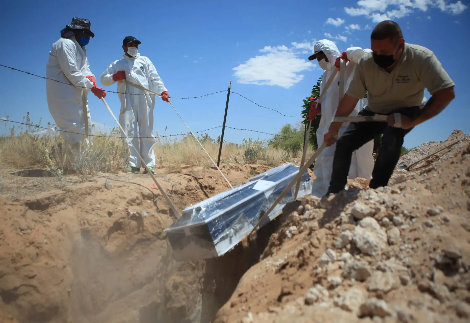 Trabajadores de una funeraria bajan un ataúd con una víctima de COVID-19 en una zona asignada especialmente para decesos por el virus en el panteón San Rafael a 30 km. de Ciudad Juárez. Foto: EFE