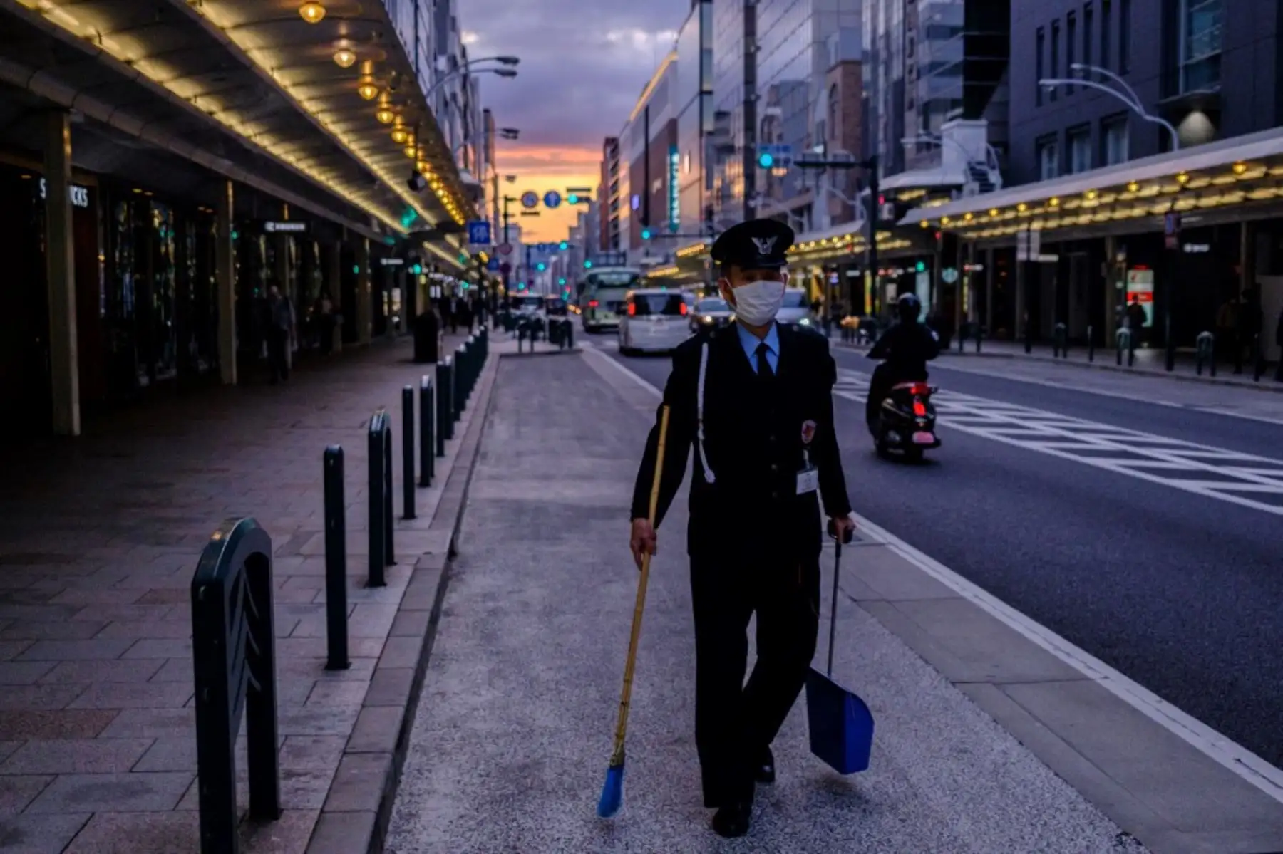 Un guardia de seguridad con una máscara facial en medio de preocupaciones por el coronavirus covid-19 camina con una escoba en Kioto 

Foto: AFP