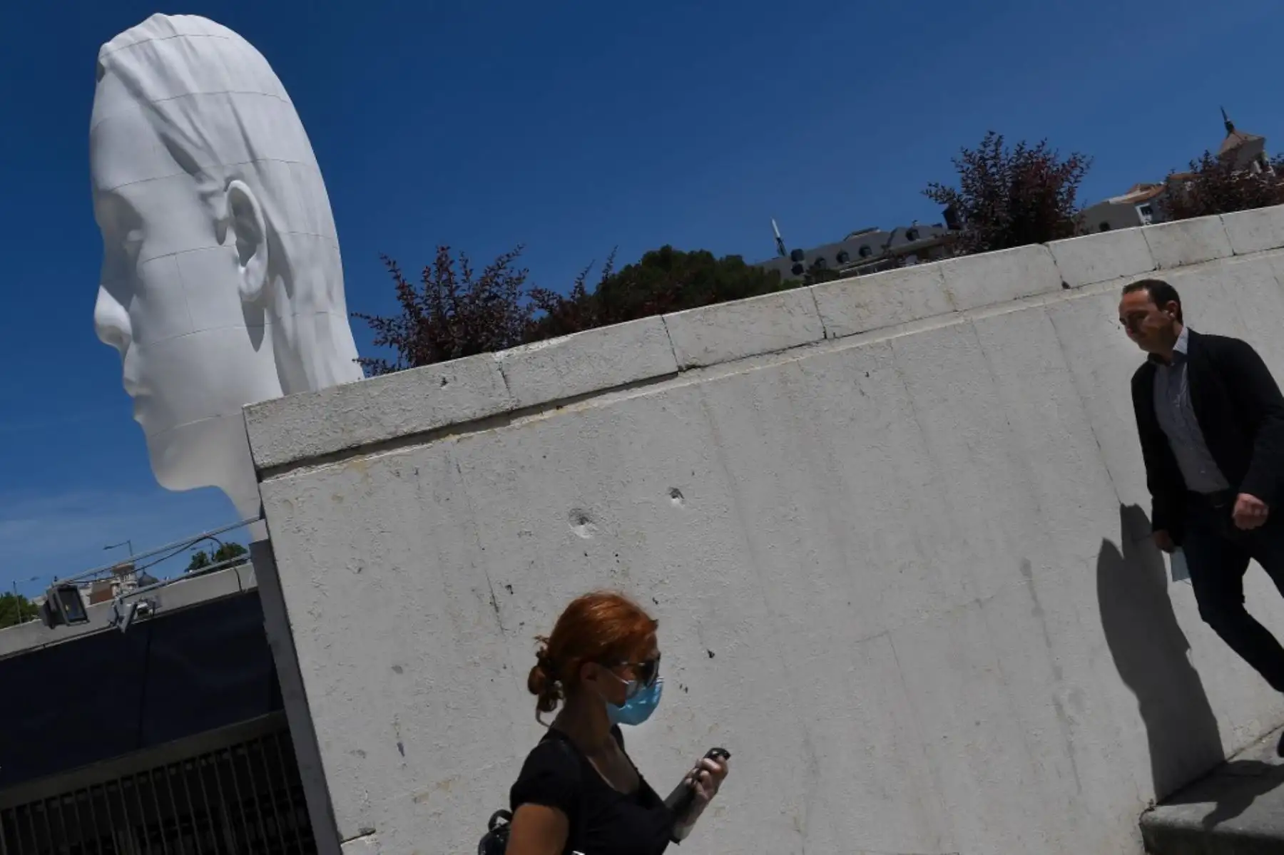 Una mujer con una máscara facial pasa junto a un hombre sin máscara cerca de la escultura "Julia" del artista español Jaume Plensa en la Plaza Colón de Madrid.
Foto: AFP