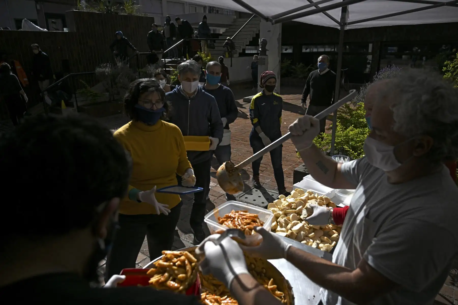 Un voluntario sirve una comida mientras la gente hace cola en un comedor popular en Montevideo. Foto: AFP
