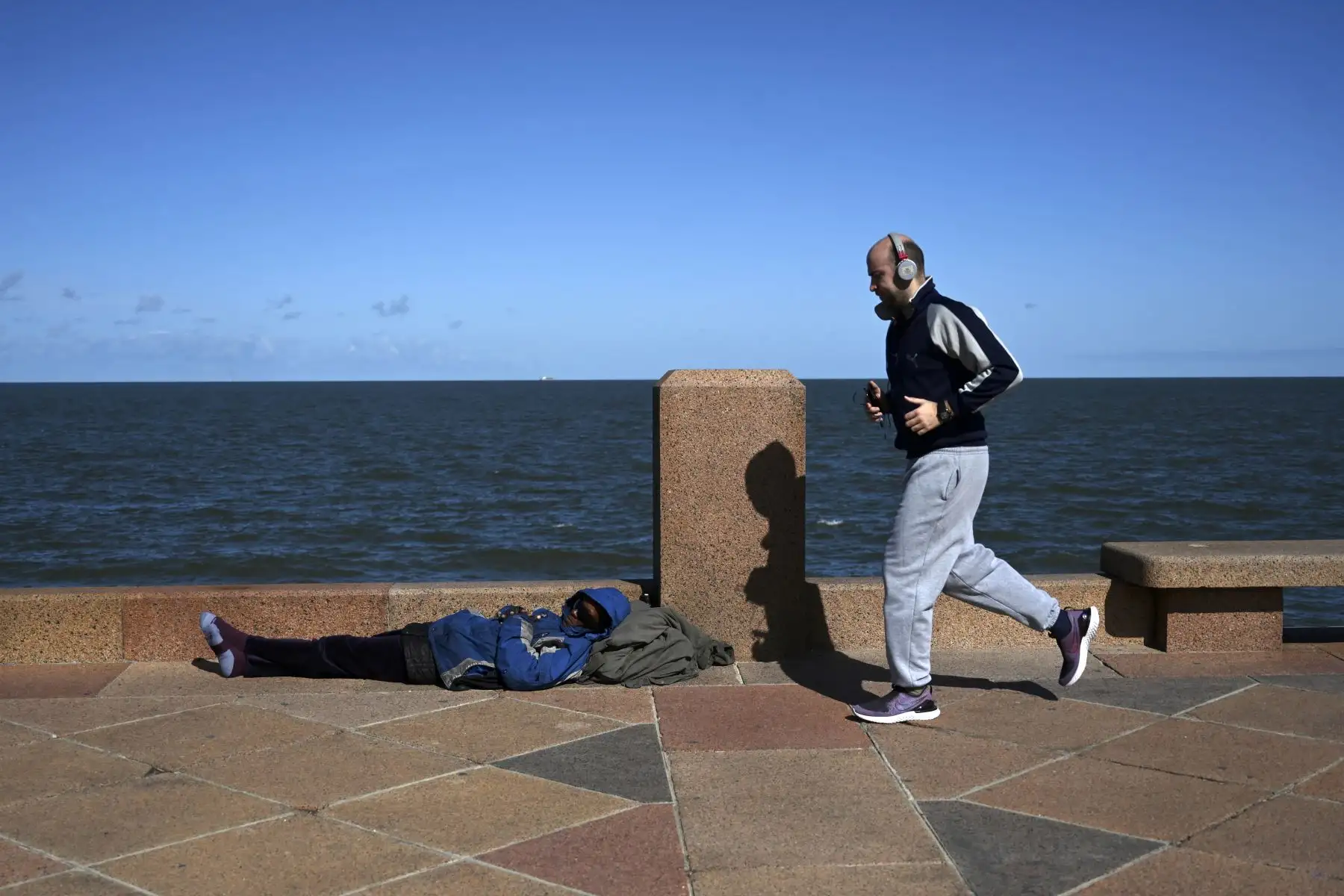 Un hombre corre y pasa junto a un hombre sin hogar a lo largo de la avenida Rambla de Montevideo. Foto: AFP