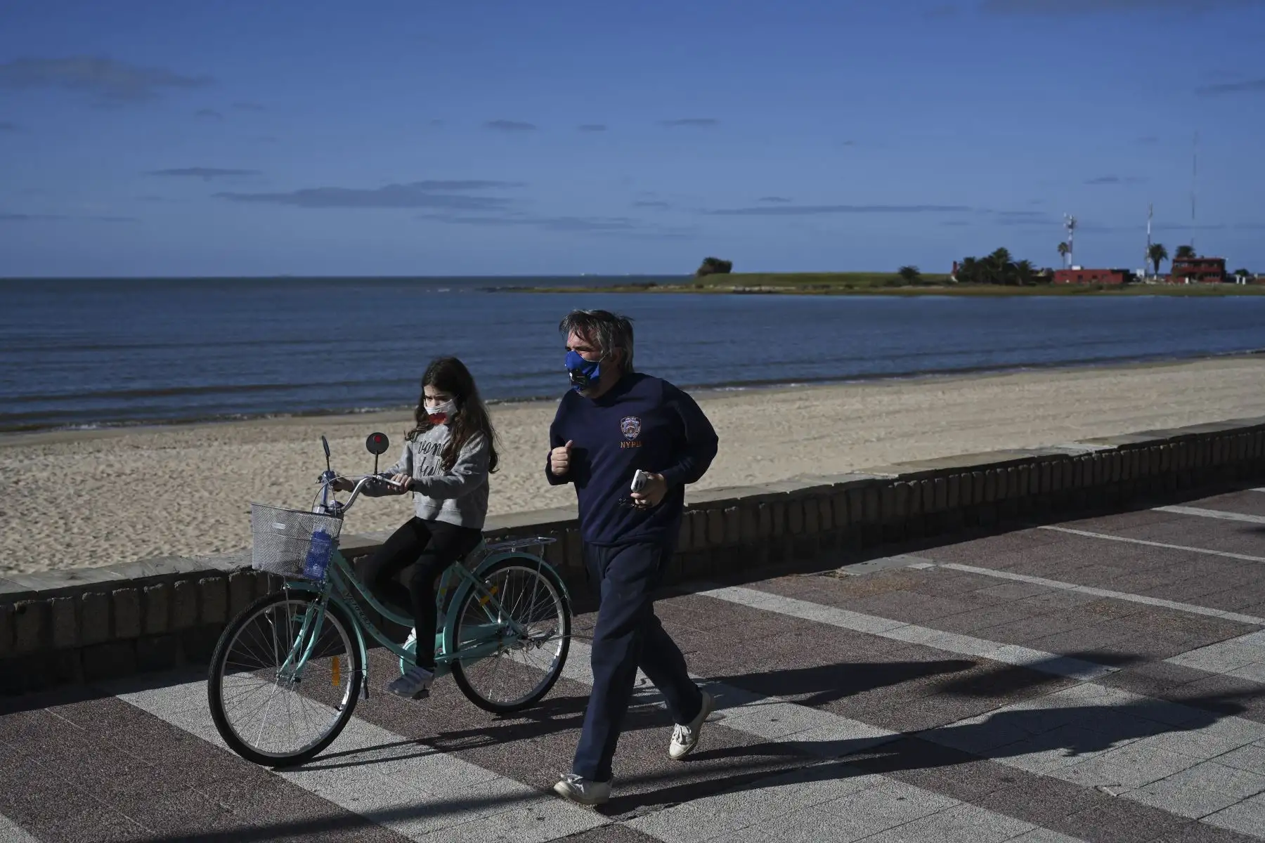 Un hombre y su hija usan máscaras faciales mientras hacen ejercicio a lo largo de la avenida costera de Montevideo Rambla. Foto: AFP