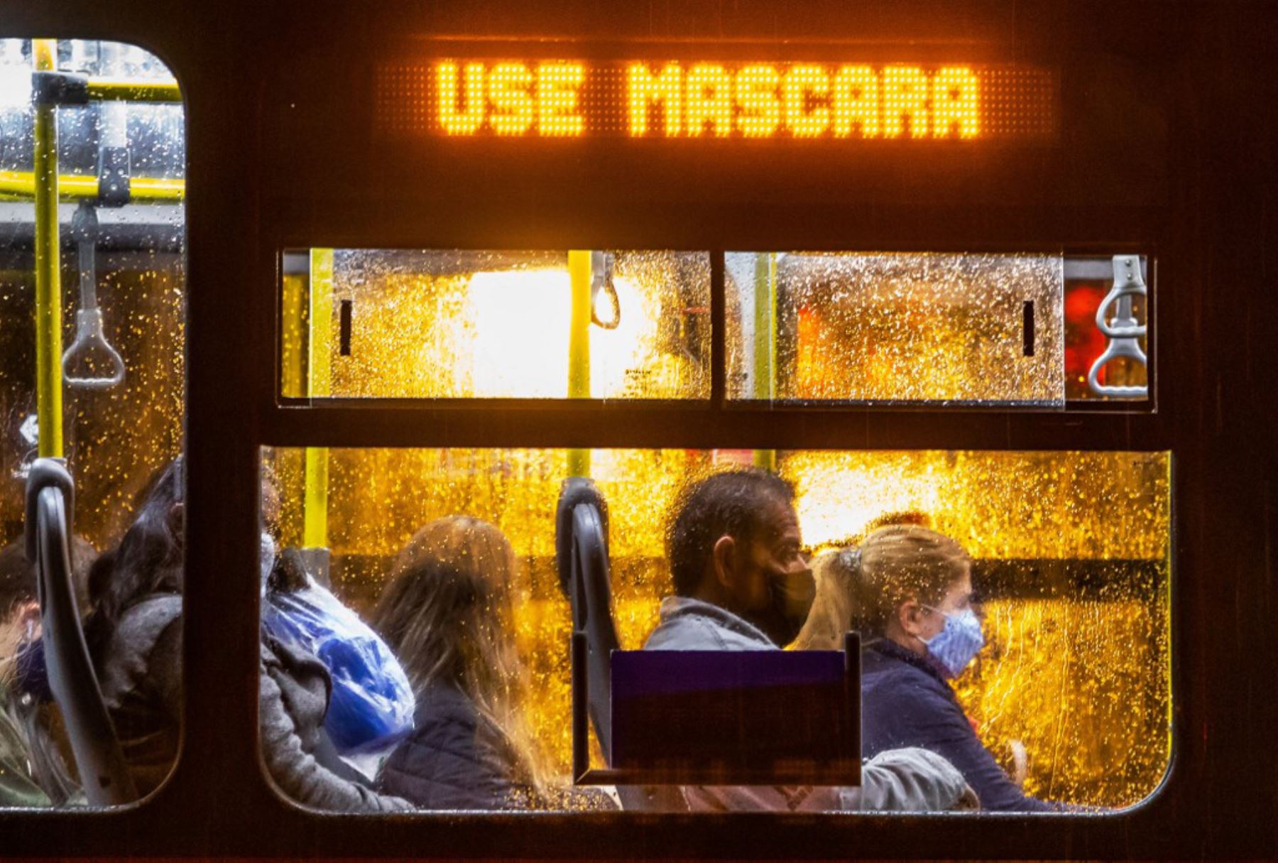 Los viajeros que usan máscaras viajan en un autobús público con un cartel electrónico que dice "Use una máscara facial", en Curitiba, Brasil. Foto: AFP