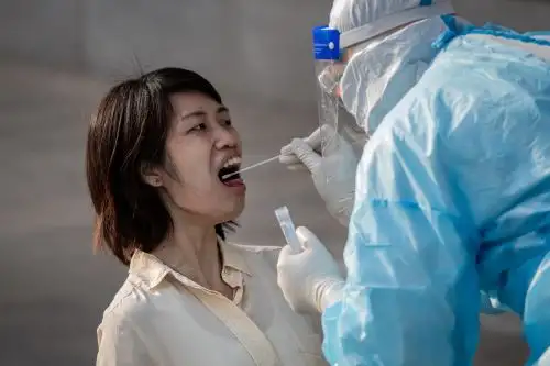 Un trabajador médico que usa equipo de protección completo toma una muestra de hisopo de una periodista para analizar el coronavirus covid-19 en China. Foto: AFP