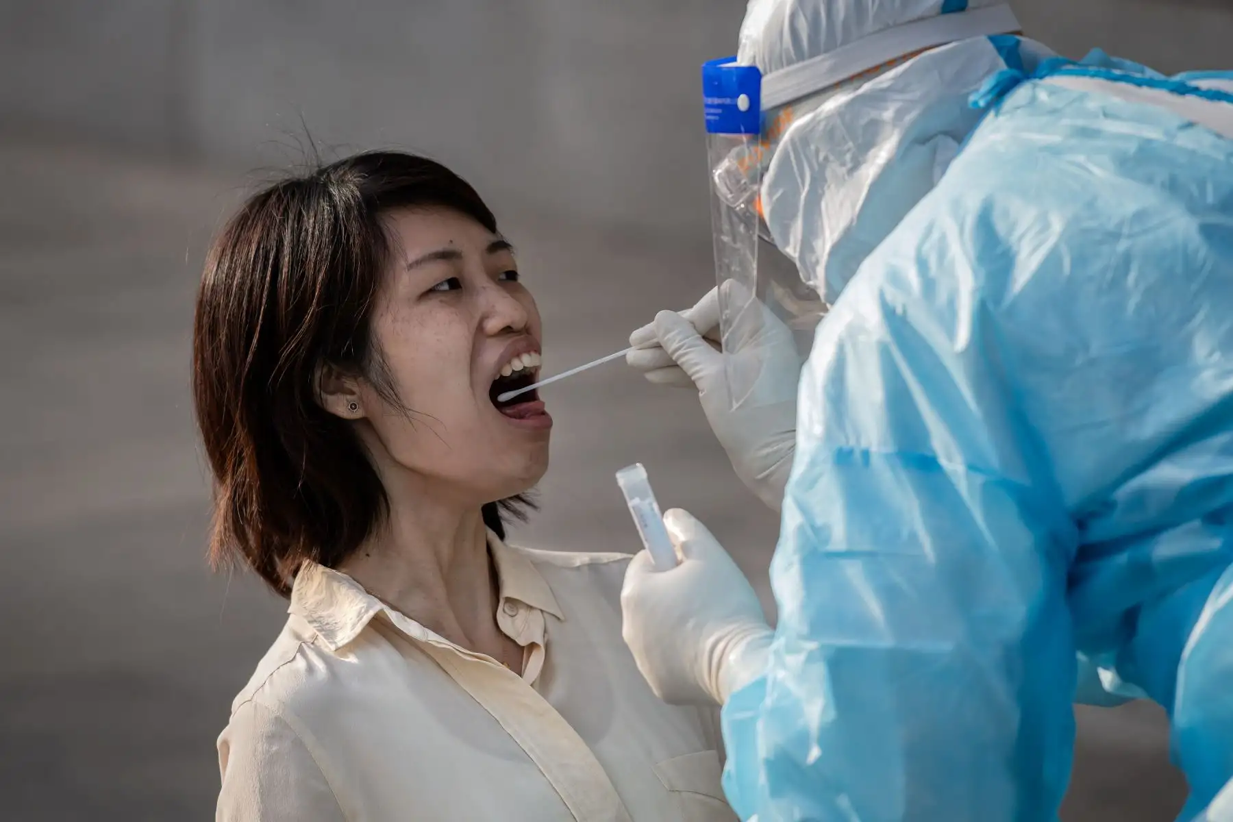Un trabajador médico que usa equipo de protección completo toma una muestra de hisopo de una periodista para analizar el coronavirus covid-19 en China. Foto: AFP