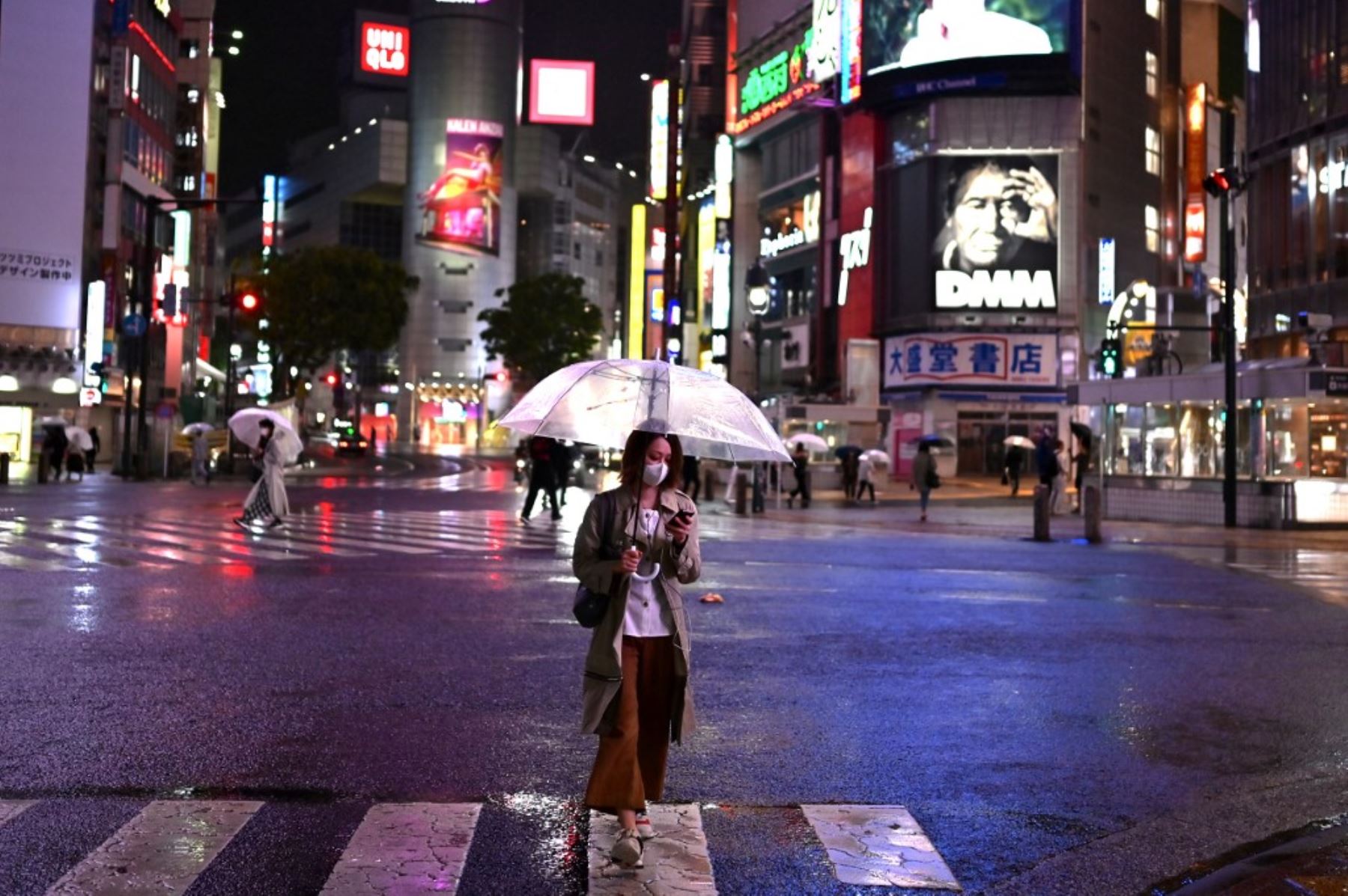 Una mujer que usa una máscara facial en medio de preocupaciones por el coronavirus COVID-19, usa un paraguas para protegerse de la lluvia mientras cruza una calle en Tokio. Foto: AFP