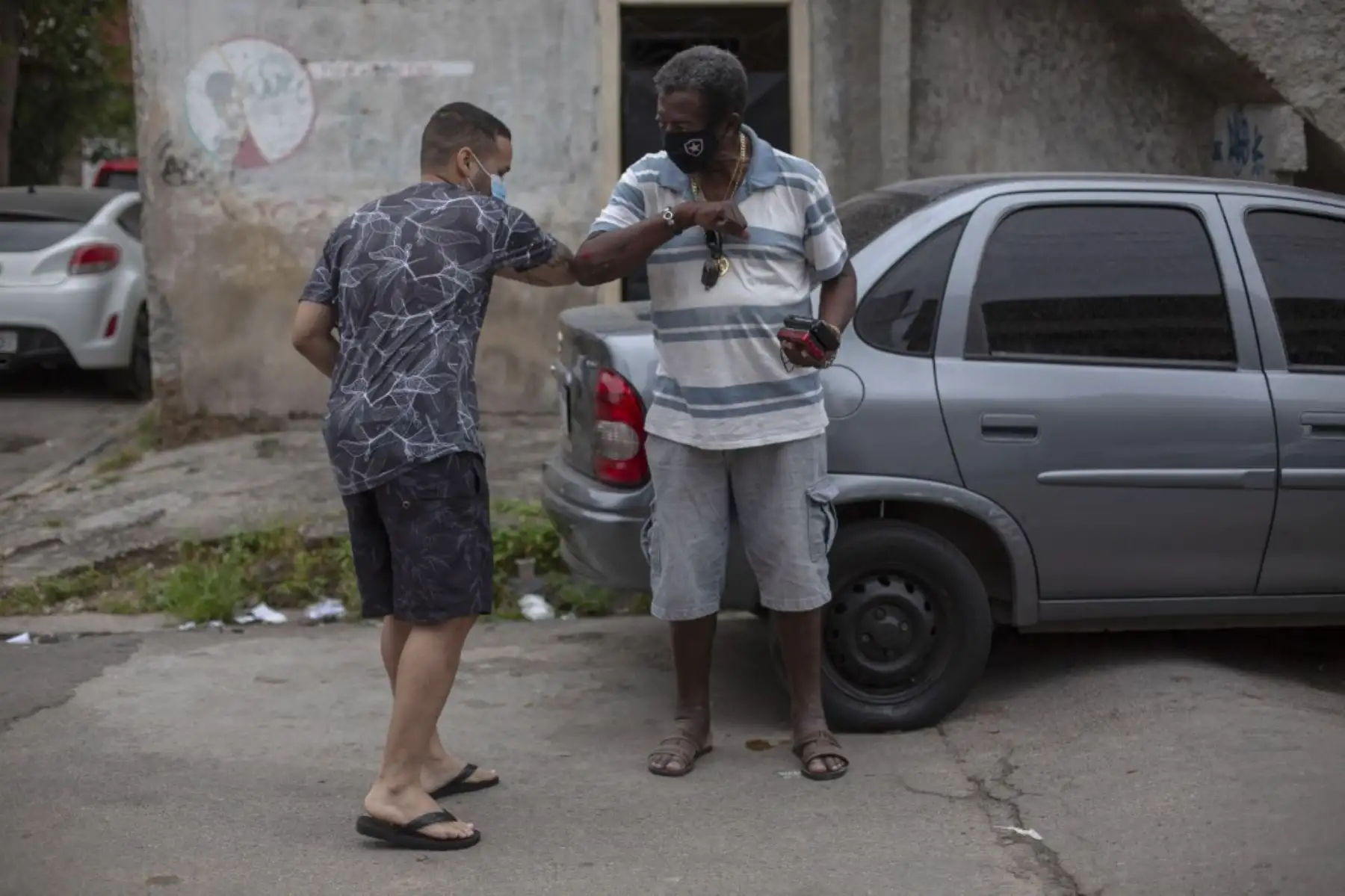 Dos hombres se saludan en la favela de Vila Vintem, fuera de la sede de la escuela de samba Unidos de Padre Miguel, mientras que los médicos realizan controles de salud gratuitos para las personas que muestran síntomas del nuevo coronavirus. Foto: AFP