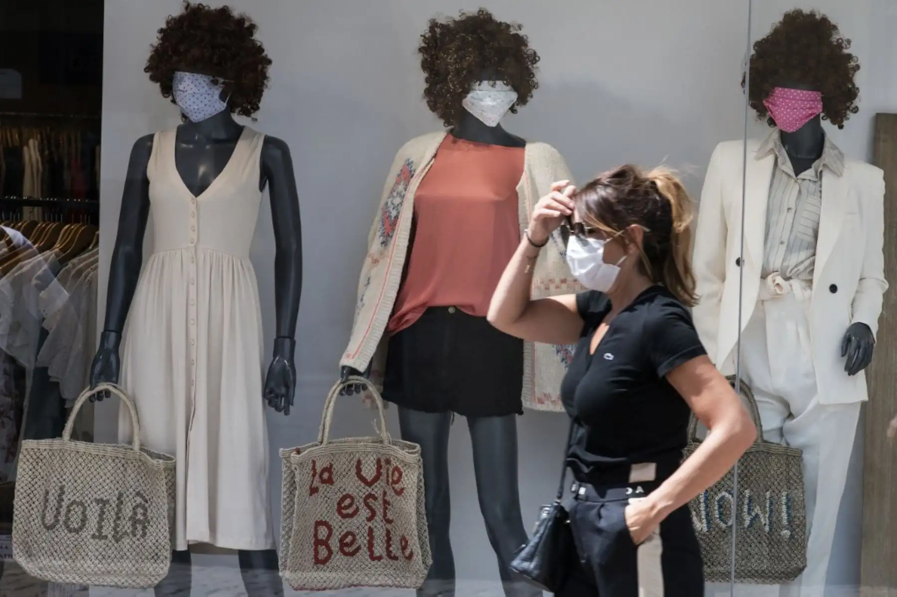 Una mujer con una máscara protectora pasa por un escaparate con maniquíes enmascarados que sostienen una bolsa en la que se lee "La vida es bella" en Mulhouse, este de Francia, Foto: AFP