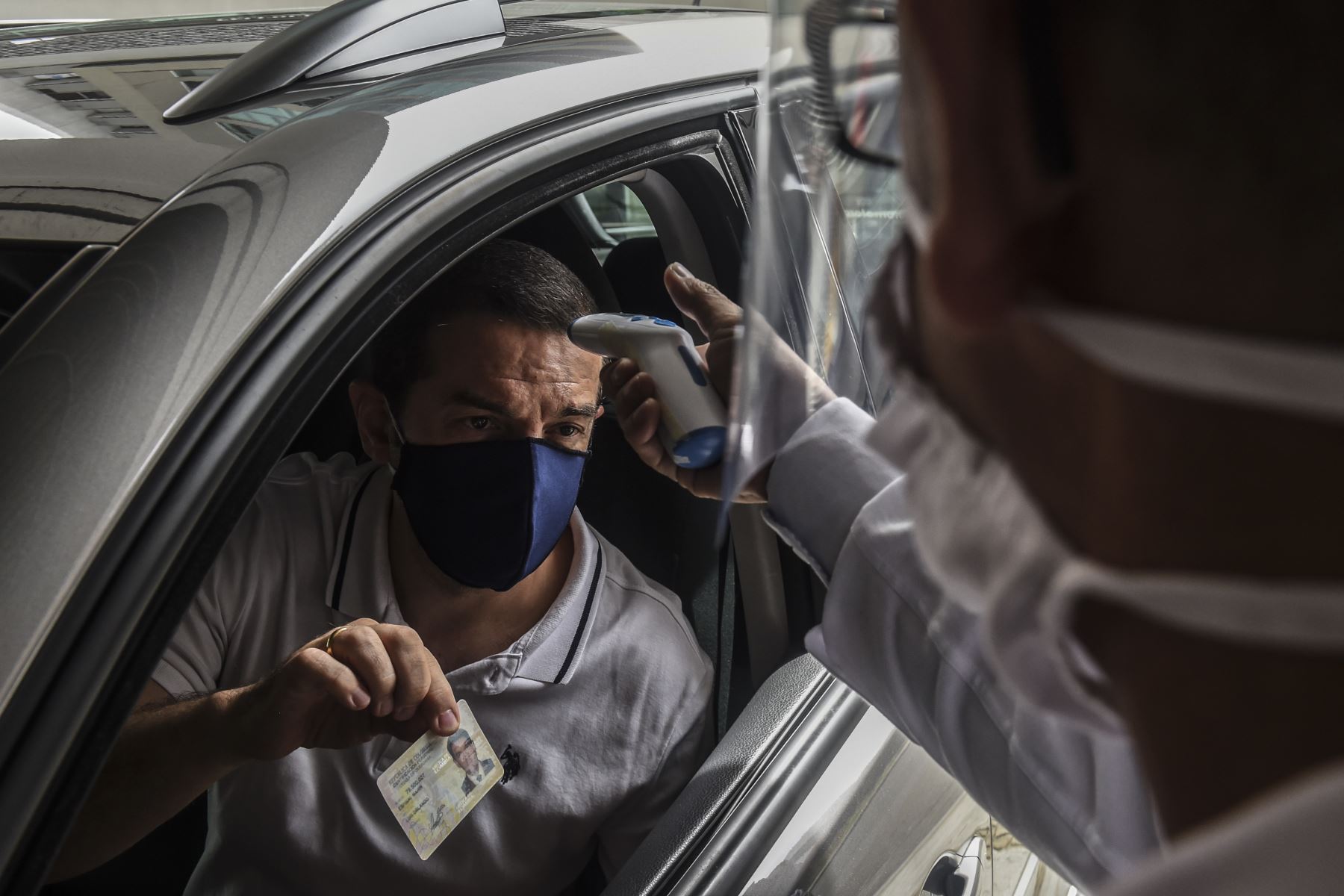 Un hombre muestra su identificación y se controla la temperatura de su cuerpo en la entrada del centro comercial, durante la nueva pandemia de coronavirus COVID-19, en Medellín. Foto: AFP