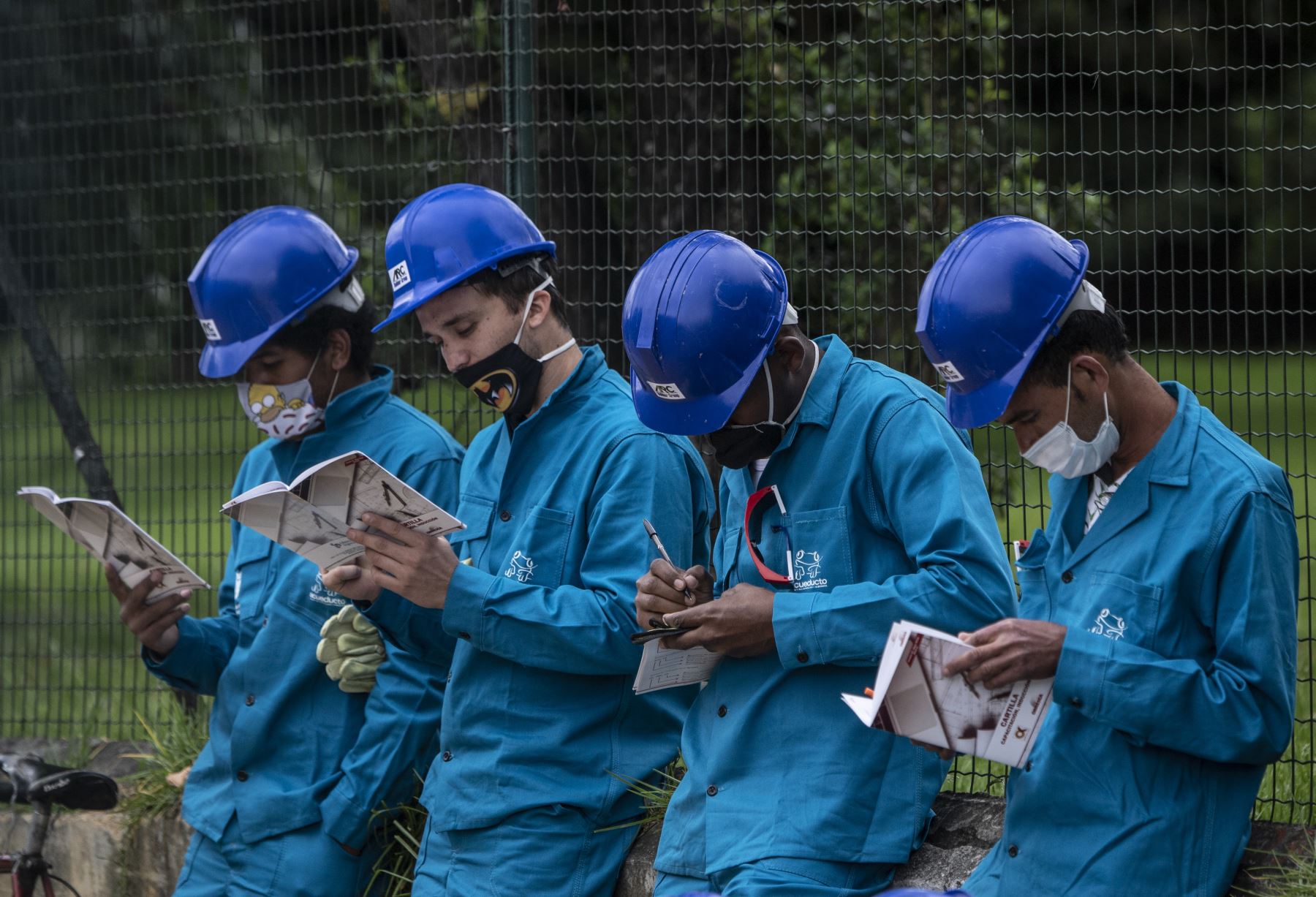 Los trabajadores de la construcción que leen usan una máscara facial, afuera de un centro comercial durante la pandemia de coronavirus COVID-19, en Bogotá. Foto: AFP