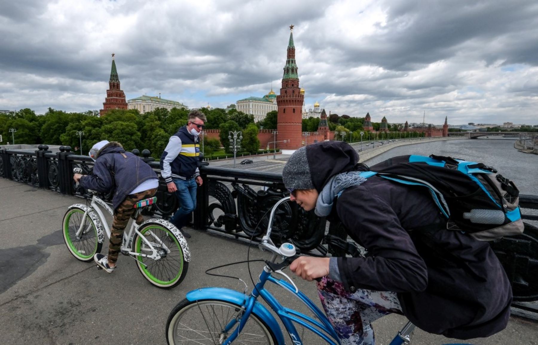 Los ciclistas pasan junto a un hombre con una máscara facial en un puente frente al Kremlin en el centro de Moscú. Foto: AFP