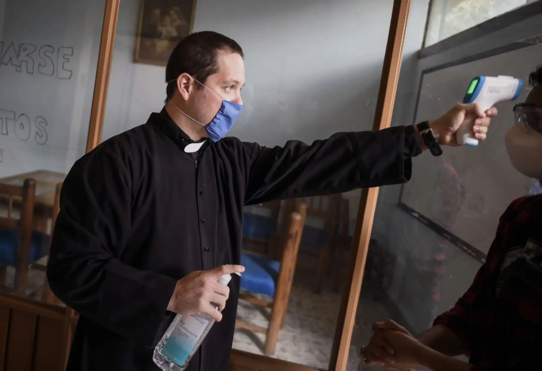 El sacerdote Esteban López usa una máscara facial mientras verifica la temperatura de las personas antes de ingresar a la Iglesia de la Sagrada Familia en la Ciudad de México. Foto: AFP