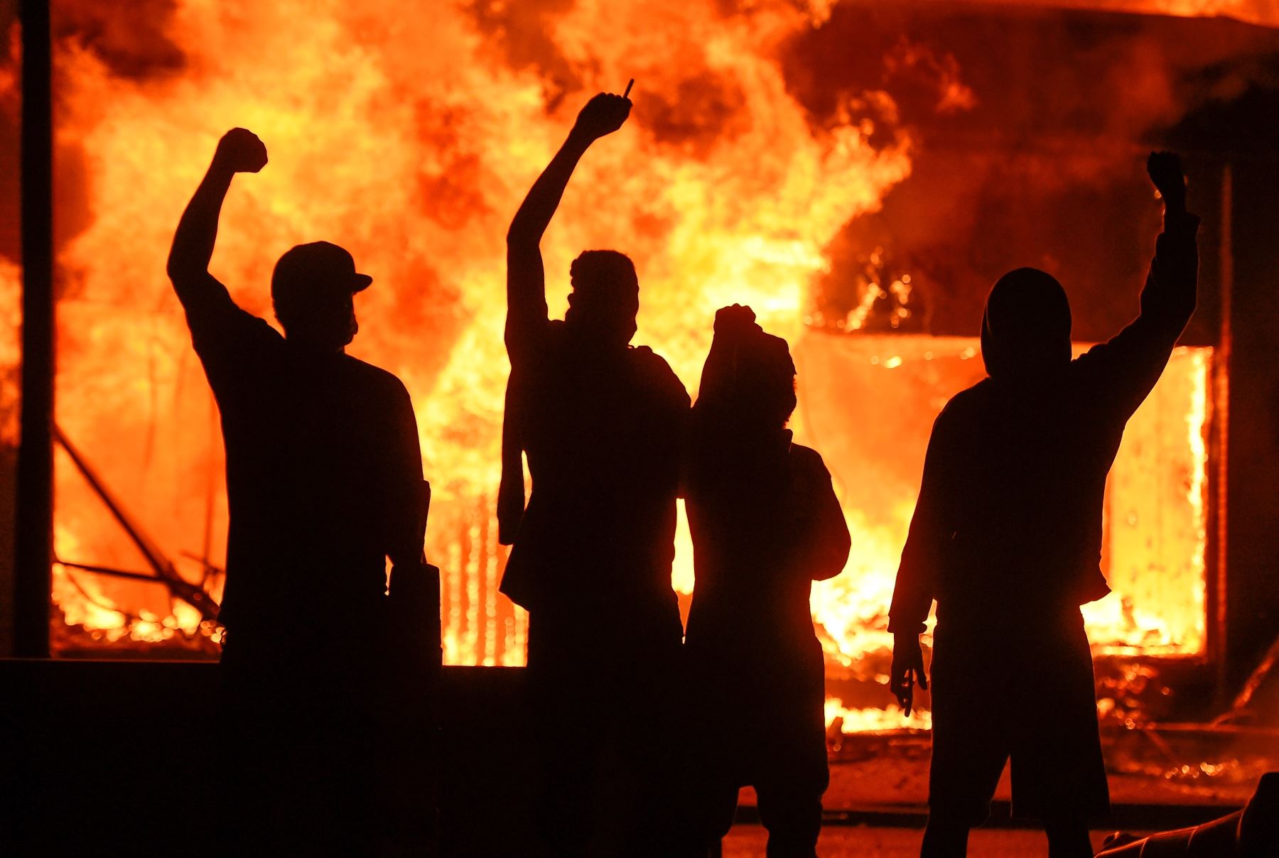 Manifestantes alzan el puño junto a una tienda en llamas, durante unos disturbios provocados tras la muerte del afroamericano George Floyd a manos de un policía el lunes pasado en Mineápolis, Minnesota, Estados Unidos. Foto: Efe.