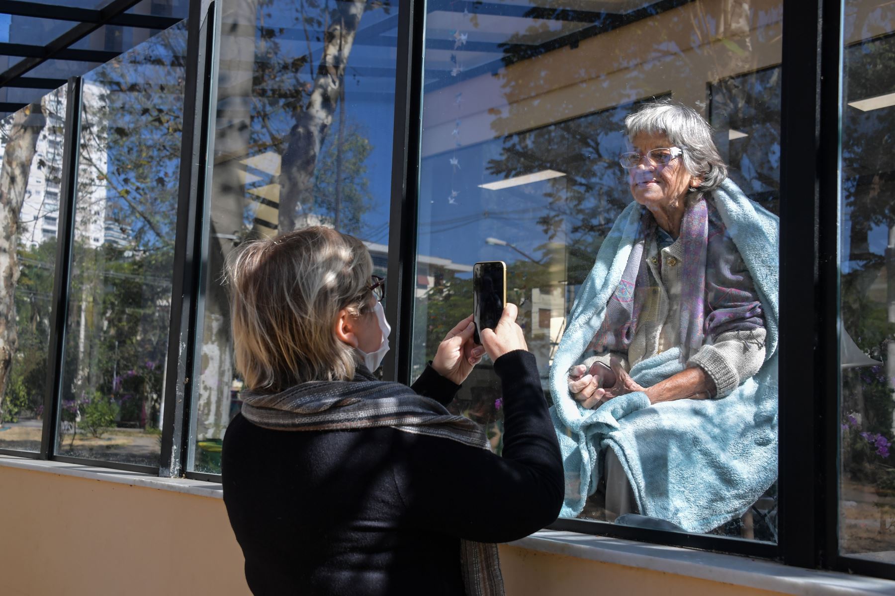 La brasileña Eunice Schleier toma una foto de su madre Olivia Schleier de 81 años a través de una ventana en el Hospital Premier, en Sao Paulo, Brasil. Foto: AFP