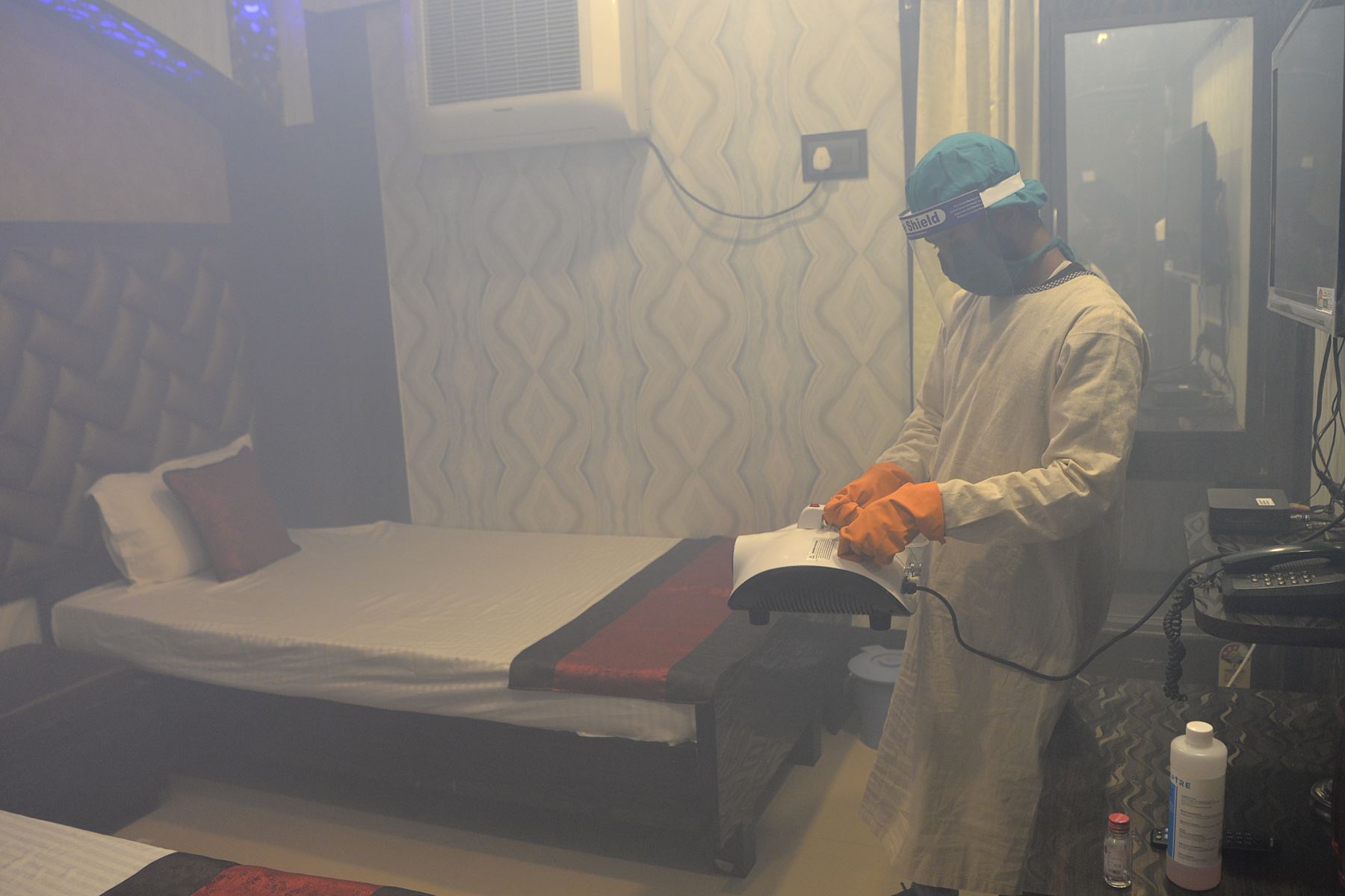 Un empleado de un hotel rocía desinfectante dentro de una habitación para las personas que necesitan someterse a una cuarentena 14 días, en la India. Foto: AFP