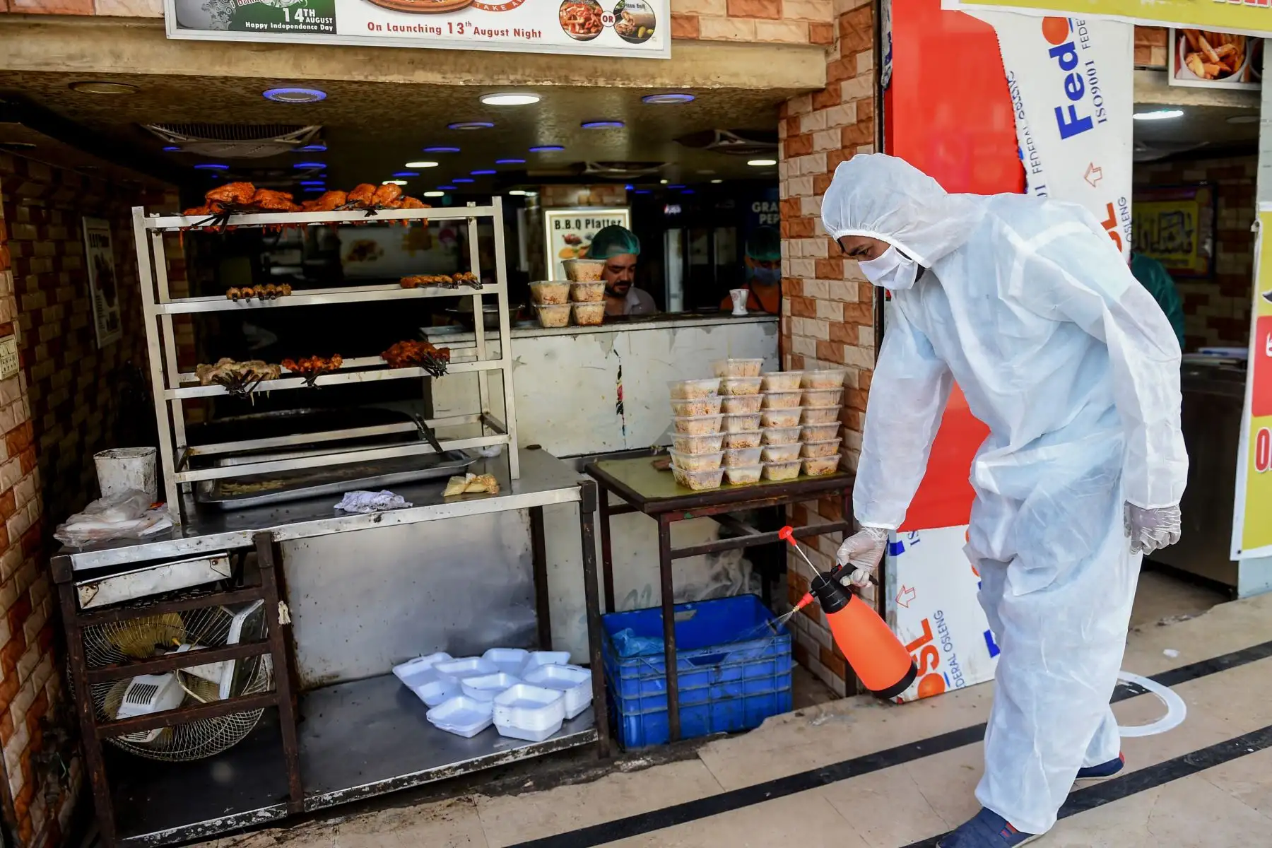 Un empleado rocía desinfectante fuera de un restaurante abierto para llevar y servicios de entrega durante un bloqueo nacional impuesto por el gobierno como medida preventiva contra el coronavirus COVID-19, en Pakistan. Foto: AFP