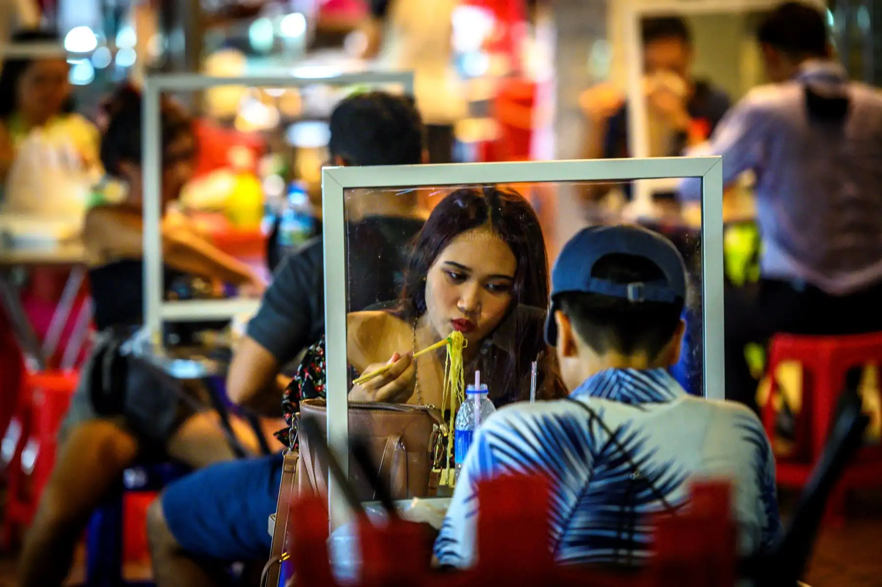 La gente come en un restaurante callejero que implementa el distanciamiento social con divisores de plástico, en Tailandia. Foto: AFP