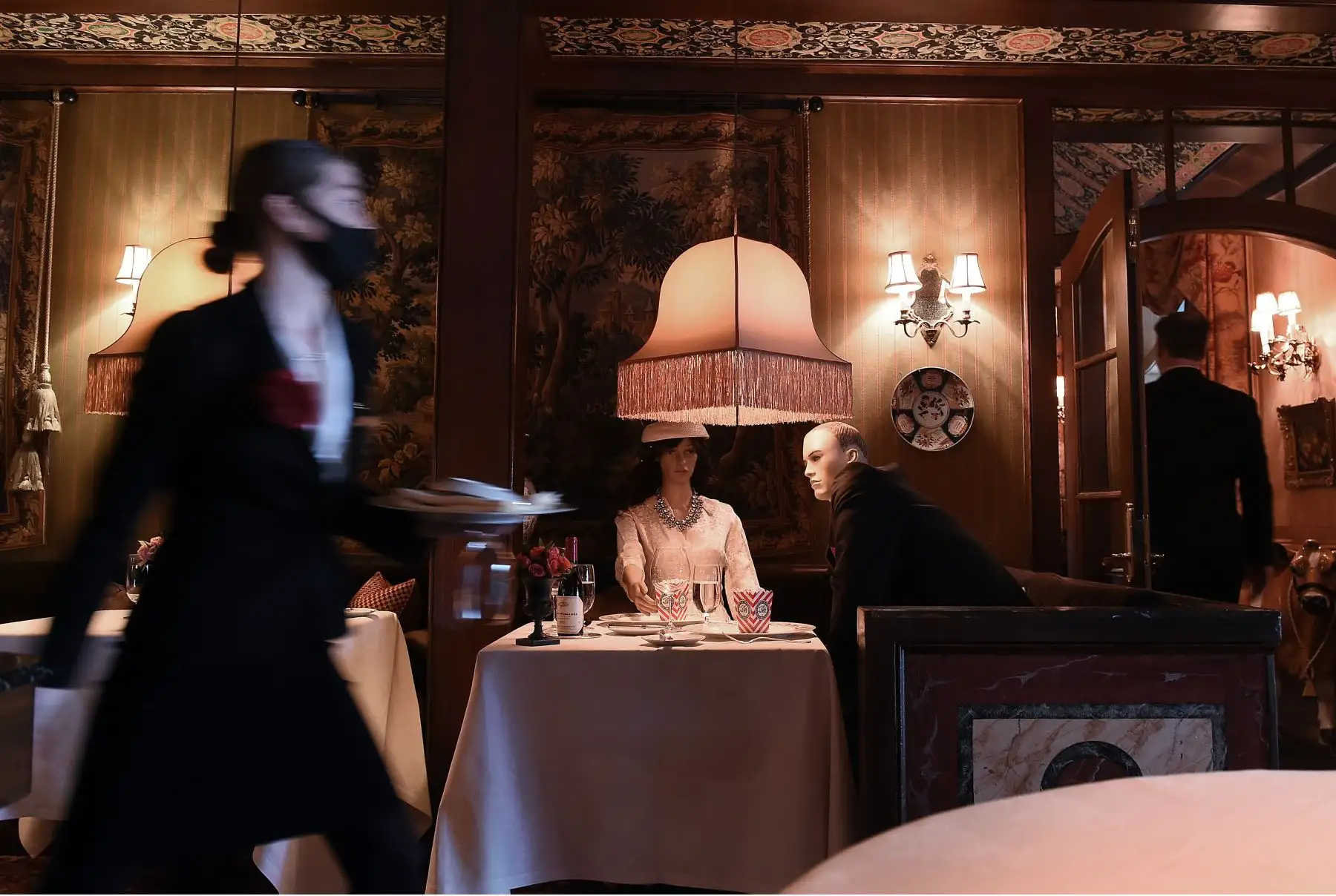 Una camarera usa una máscara facial cuando pasa delante de los maniquíes que pueblan el comedor de The Inn at Little Washington, uno de los restaurantes más reconocidos del país. Foto: AFP