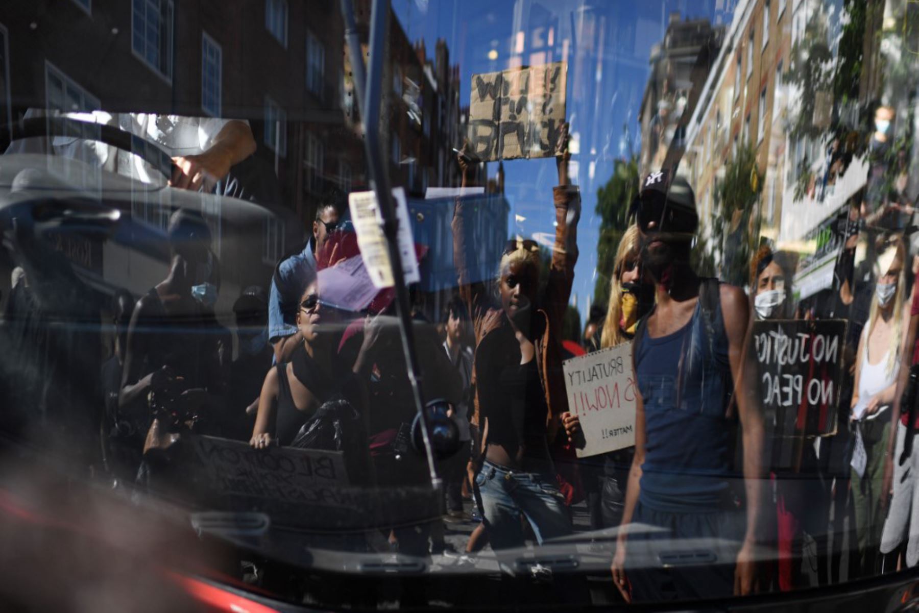 Manifestantes se reflejan en el parabrisas de un autobús  que bloquea la calle en Sloane Square, en Londres el 31 de mayo de 2020 después de marchar a la embajada de los Estados Unidos para protestar por la muerte de George Floyd. Foto: AFP