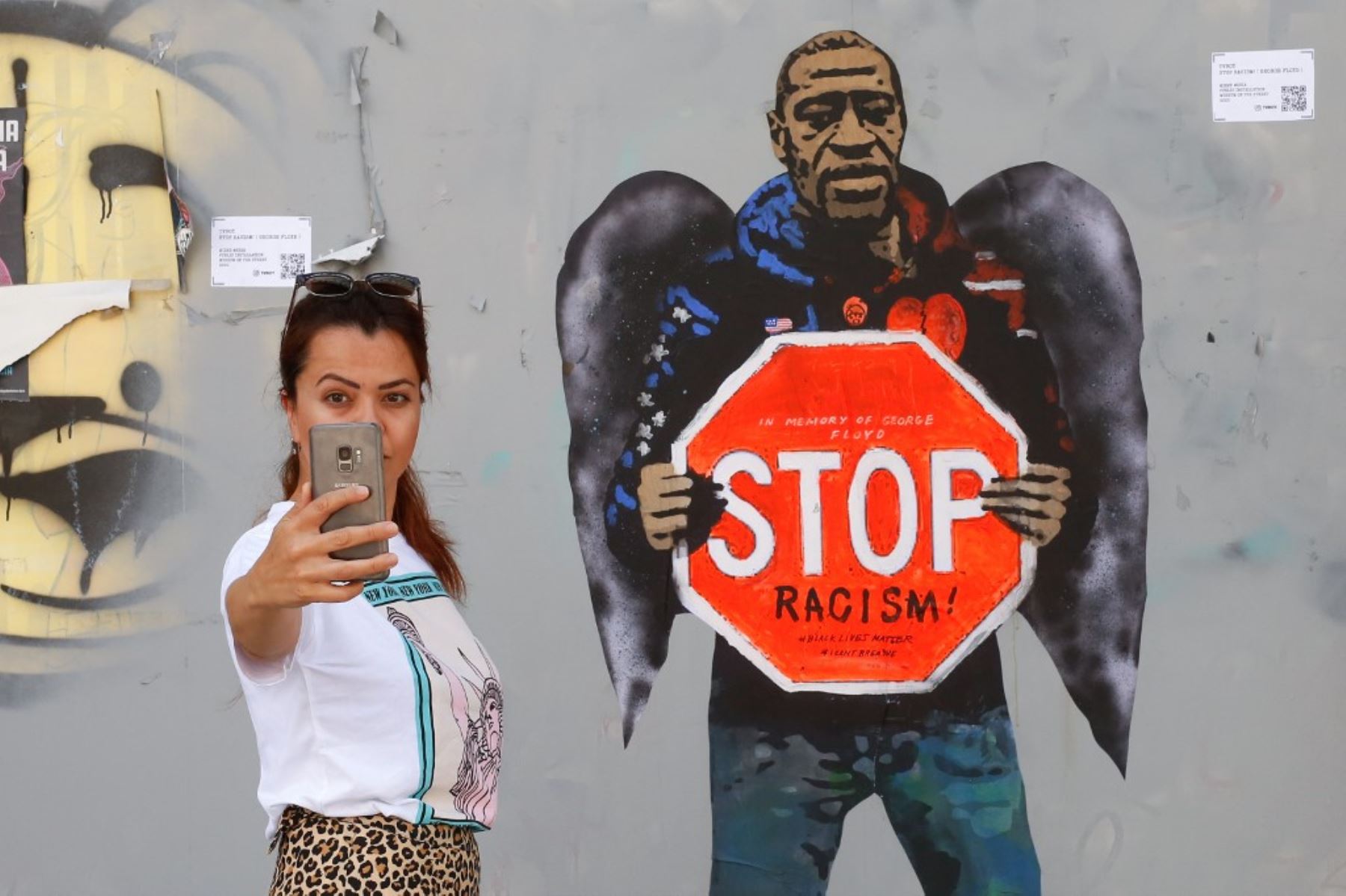 Una mujer toma una foto selfie posando junto a un mural que representa a George Floyd con alas de ángel y con una señal de alto contra el racismo, en una calle de Barcelona el 31 de mayo de 2020. Foto: AFP
