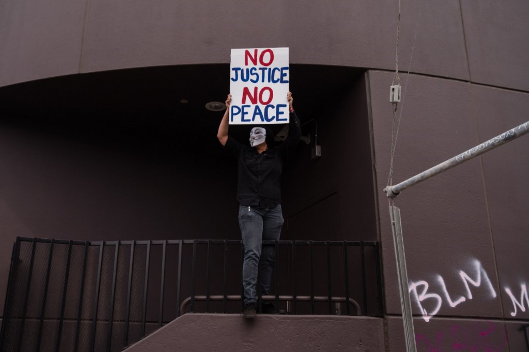 Un manifestante con una máscara de Guy Fawkes sostiene un cartel que dice "No Justice No Peace" en Los Ángeles el 30 de mayo de 2020 luego de una protesta contra la muerte de George Floyd. Foto: AFP