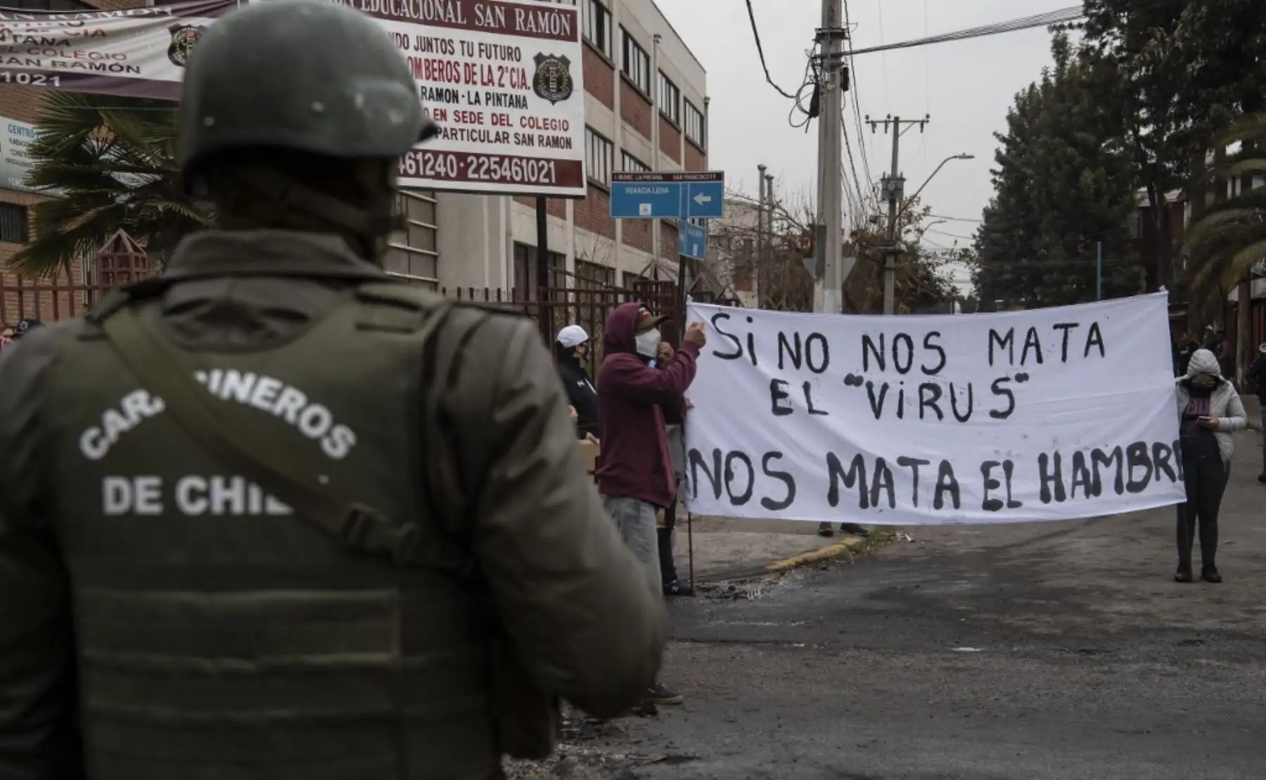 Un policía mira a las personas con un cartel que dice "Si el virus no nos mata, el hambre sí" para protestar por no obtener ayuda del gobierno. Foto: AFP