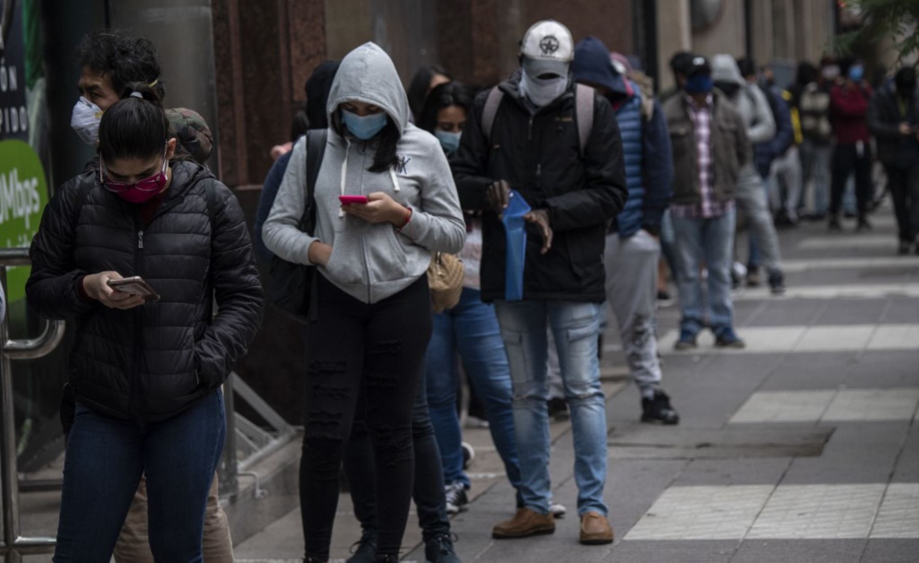 Las personas usan máscaras faciales mientras hacen cola para obtener un seguro de desempleo fuera de la sede de la Administración de Fondos de Desempleo de Chile en Santiago. Foto: AFP