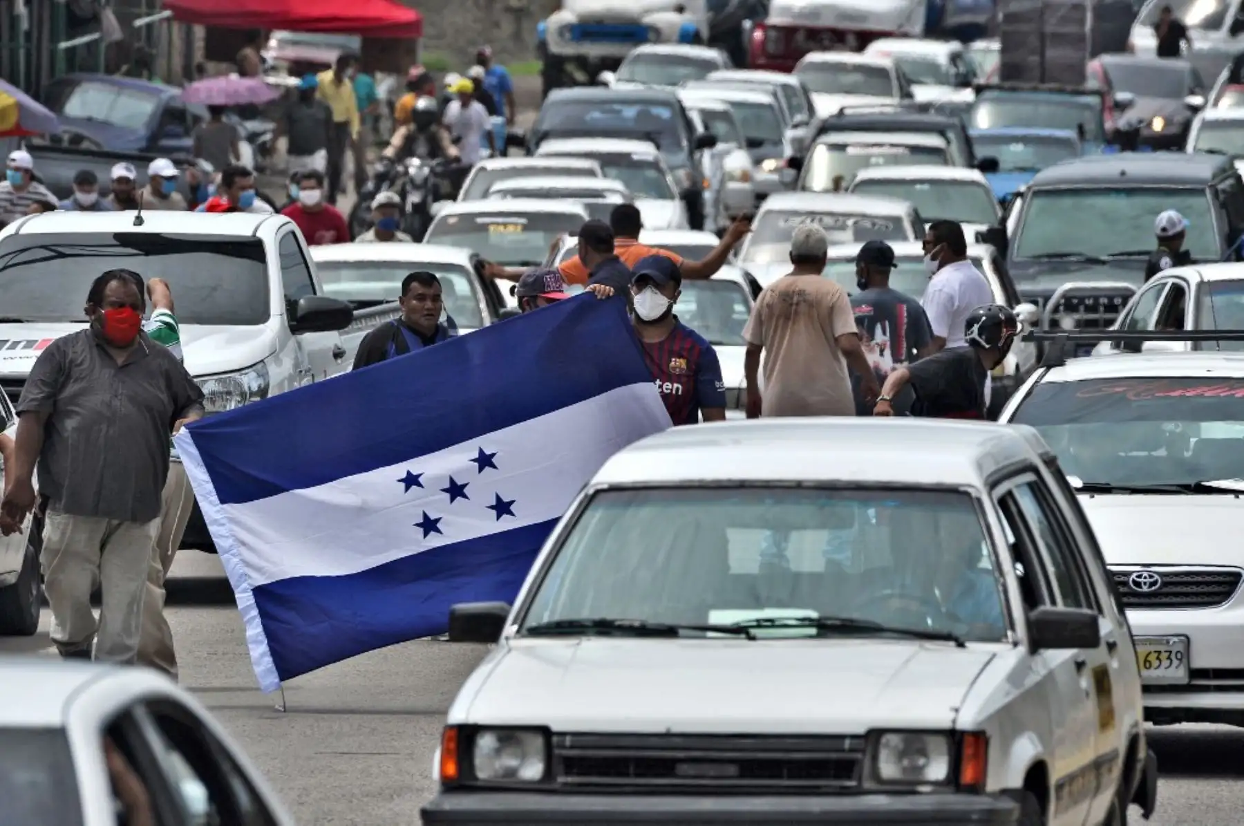 Los taxistas sostienen una bandera hondureña mientras bloquean un camino para protestar por la demanda de alimentos y ayuda económica en Tegucigalpa. Foto: AFP