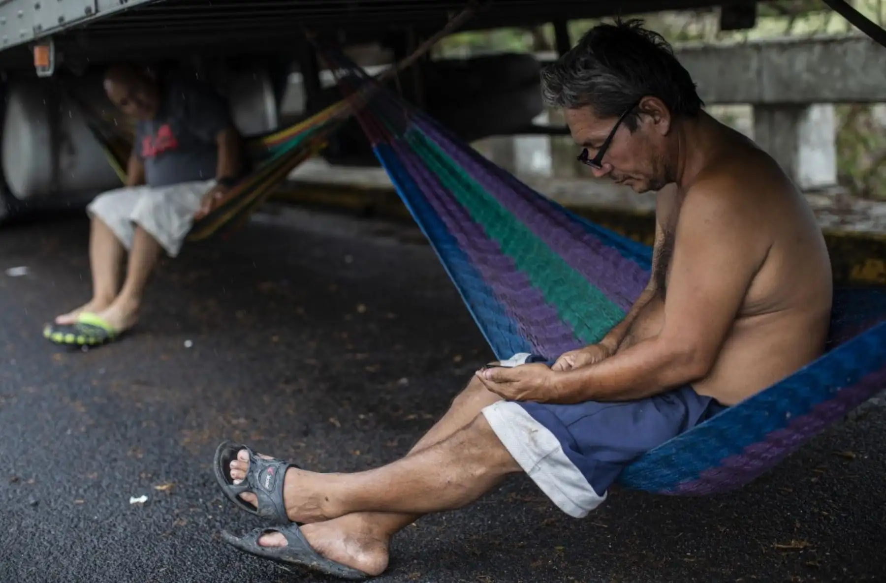 Un camionero revisa su teléfono sentado en una hamaca atada debajo de un camión durante un bloqueo en la frontera de Peñas Blancas entre Nicaragua y Costa Rica, en Rivas, Nicaragua. Foto: AFP