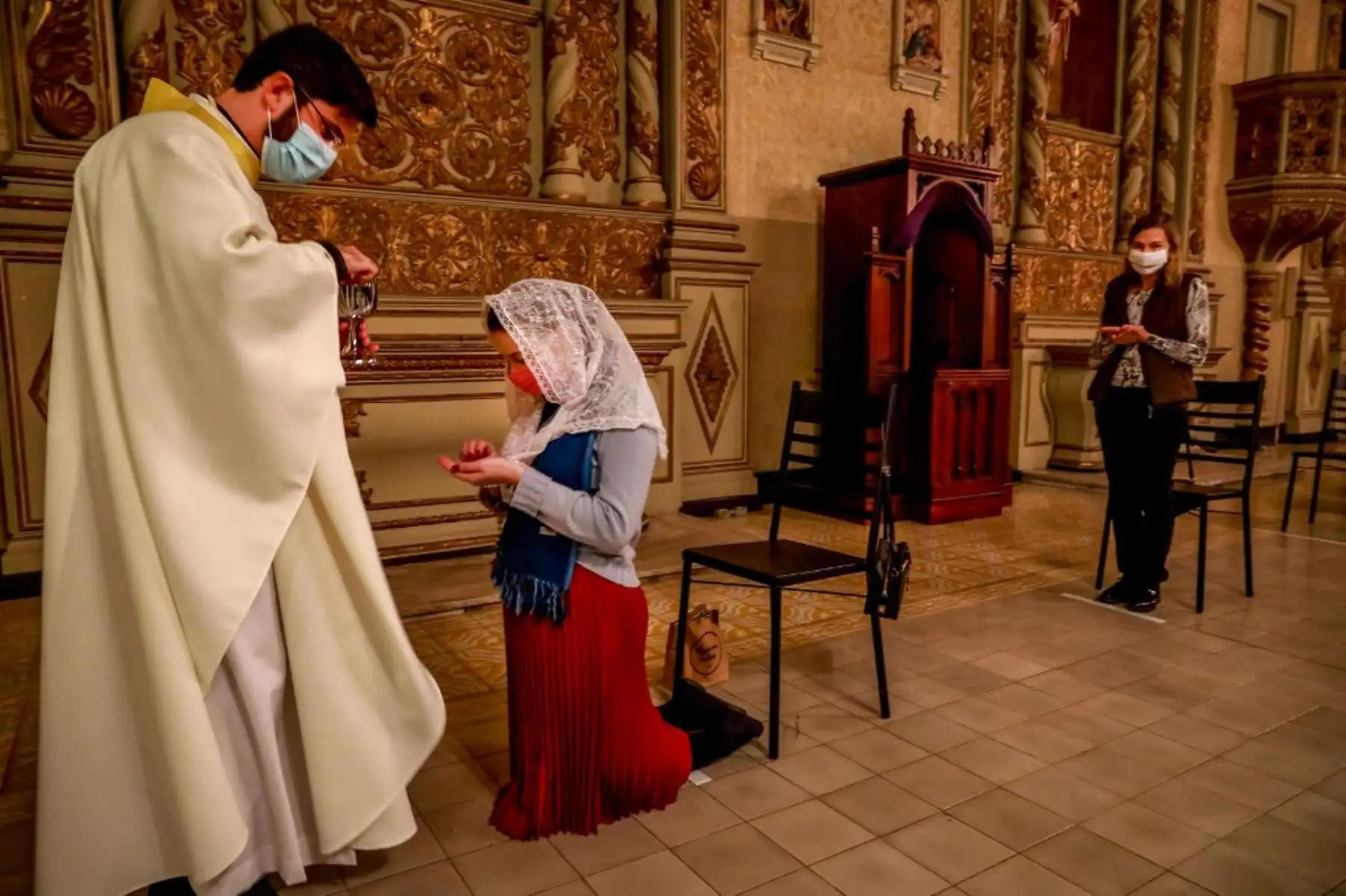 El sacerdote Lucas Mendes, con una máscara protectora, da la comunión a una  mujer durante la misa en la iglesia Nossa Senhora das Dores en Porto Alegre, en el sur de Brasil. Foto: AFP