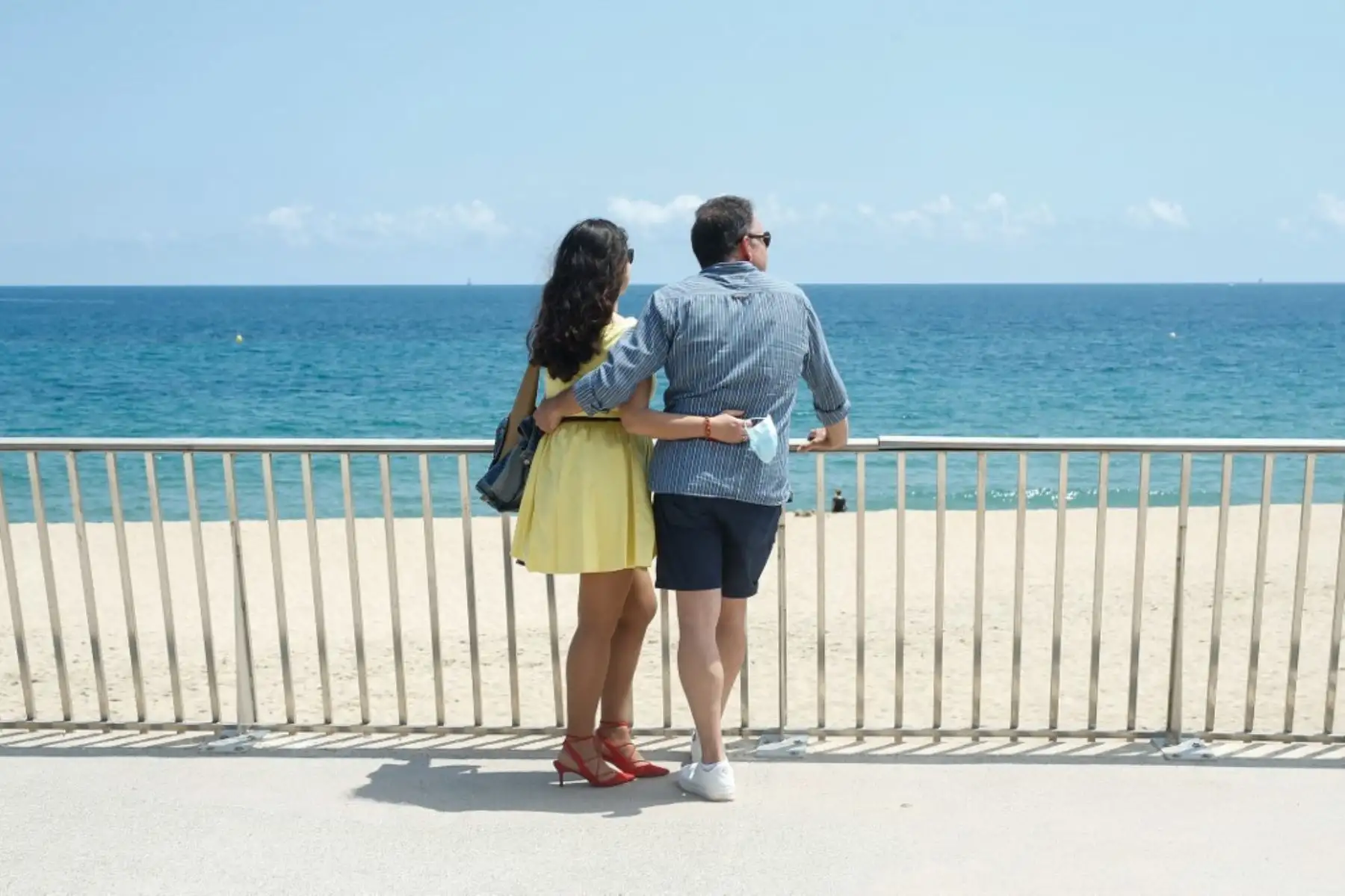 Una mujer sostiene su máscara facial mirando al mar con su pareja en Barcelona, mientras el país comienza a reaperturar las actividades en España. Foto: AFP