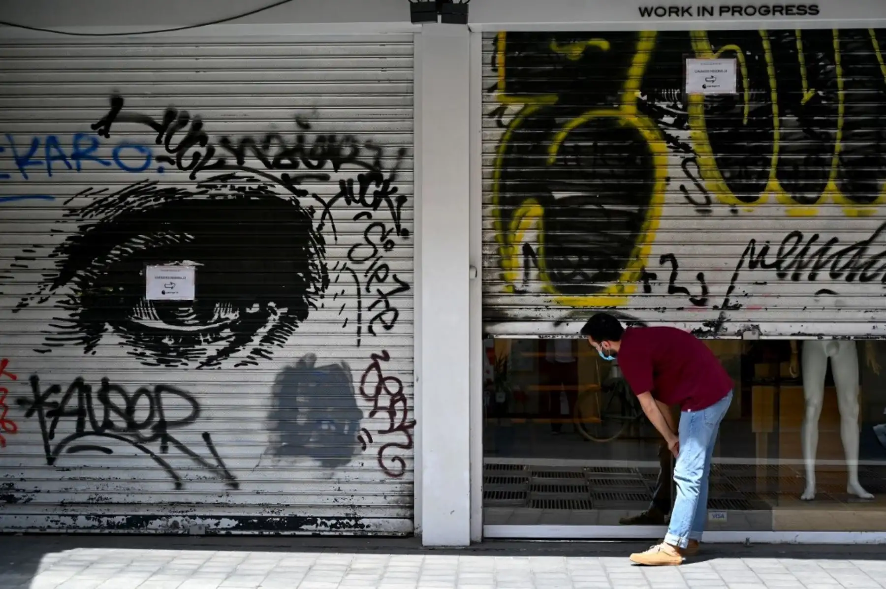Un hombre comprueba si una tienda de ropa se abrirá ya que la puerta de persiana metálica está medio cerrada, en Madrid. Foto: AFP