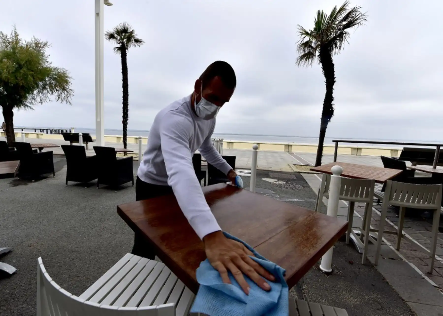 Un camarero con una máscara desinfecta una mesa en una terraza de un restaurante en Arcachon. Foto: AFP
