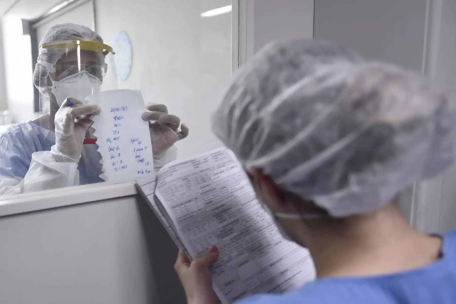 Un profesional de la salud que usa EPP completo  pasa información sobre un paciente COVID-19 a través de una ventana en la Unidad de Cuidados Intensivos (UCI) del hospital Santa Casa en Belo Horizonte, Brasil. Foto: AFP