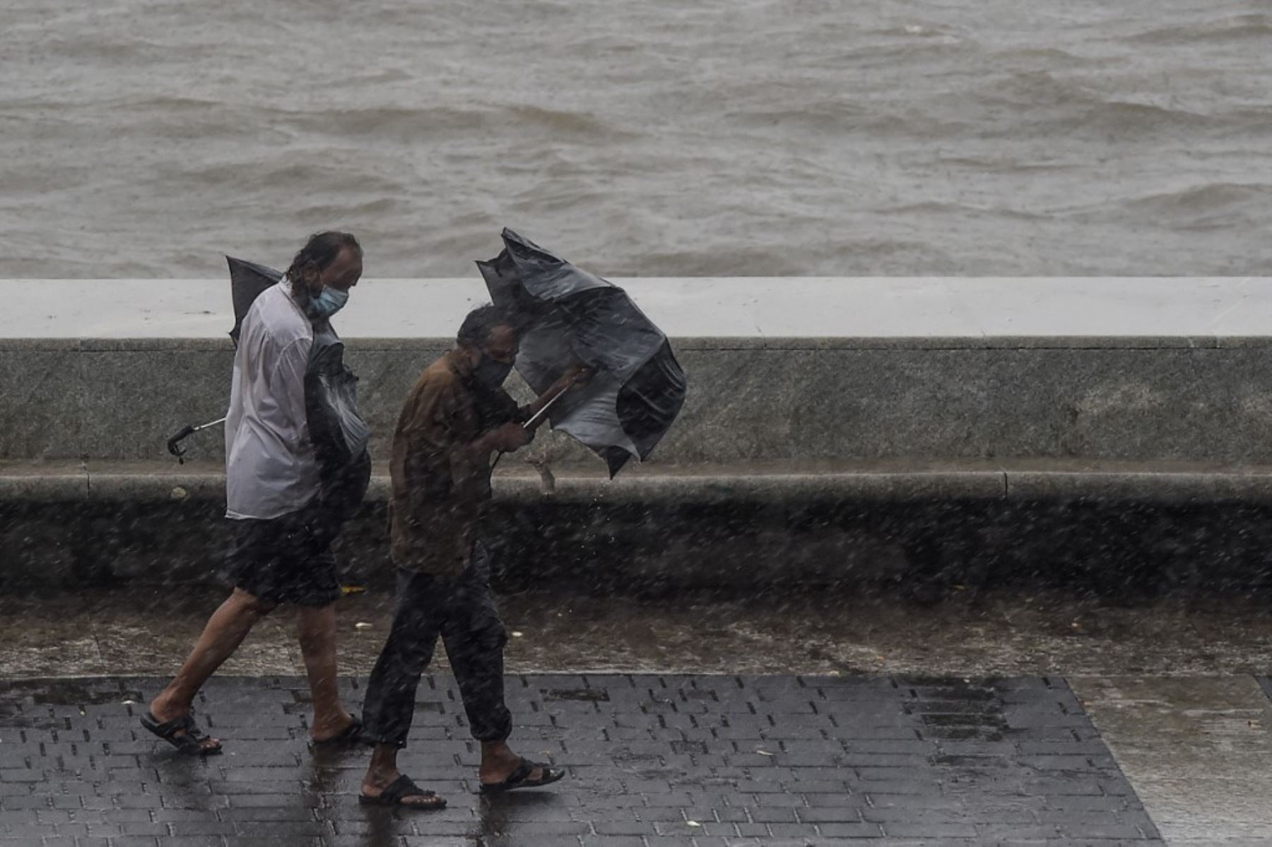 Dos hombres que llevan paraguas caminan en Marine Drive bajo una fuerte lluvia en Mumbai mientras el ciclón Nisarga avanza hacia la costa occidental de la India.