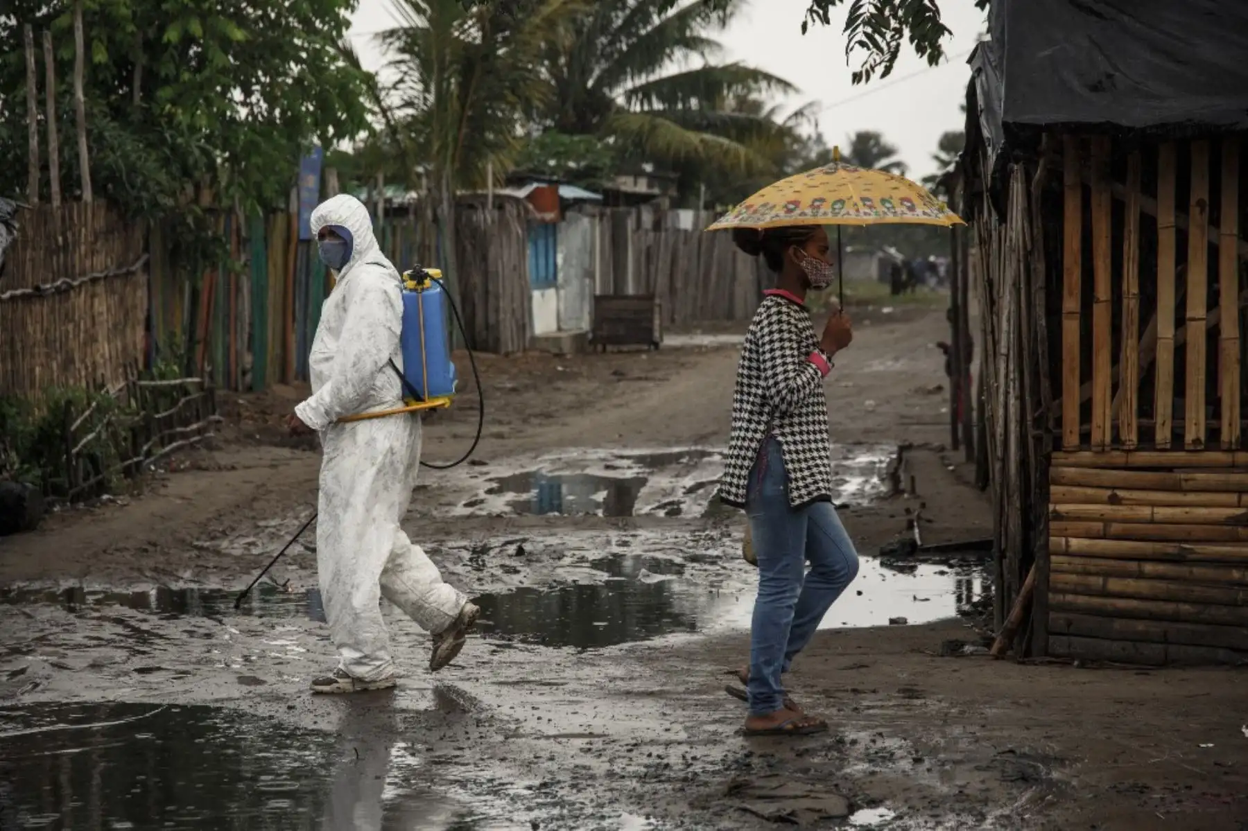 Una mujer se protege de la lluvia cuando un funcionario del Ministerio de Salud rocía desinfectante en Toamasina, una importante ciudad portuaria en la costa este de Madagascar. Foto: AFP