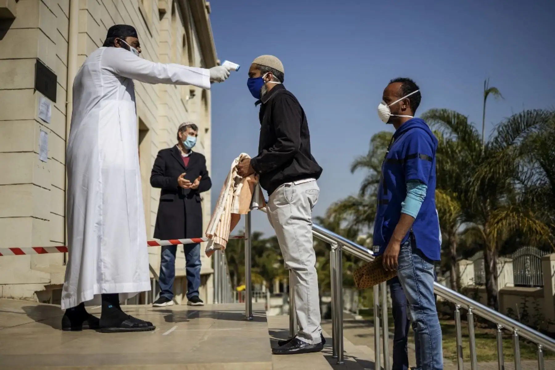 A un hombre que lleva una estera de oración y usa una máscara como medida preventiva contra el coronavirus COVID-19 se le revisó la temperatura en la entrada de la mezquita de Nizamiye antes de la oración del viernes en Midrand, Johannesburgo. Foto: AFP