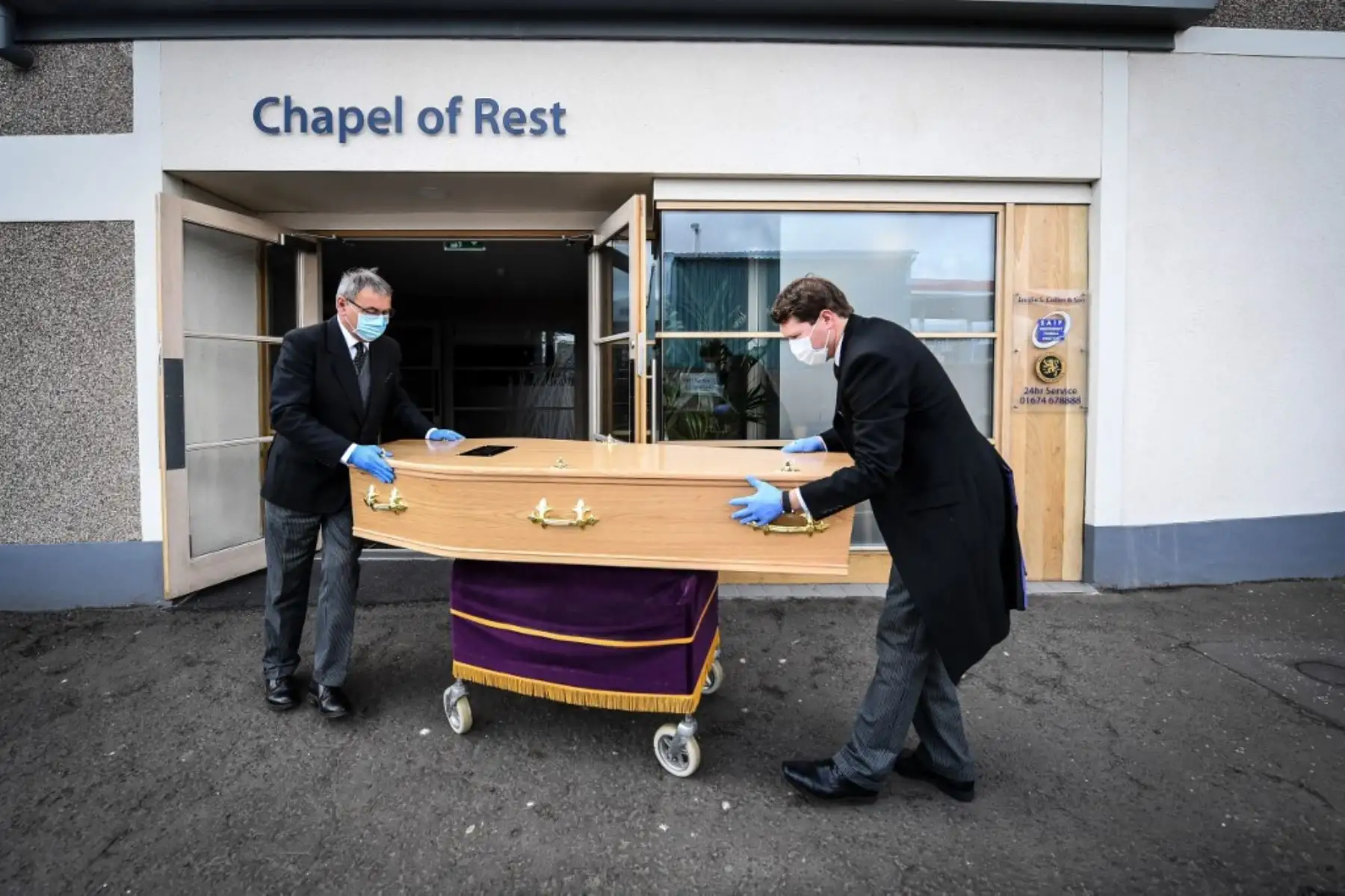 Los directores de funerales James Collier y David Bell con máscara y guantes transportan el ataúd de la cuidadora Janet Livingston, de 60 años, quien murió de COVID-19. Foto: AFP