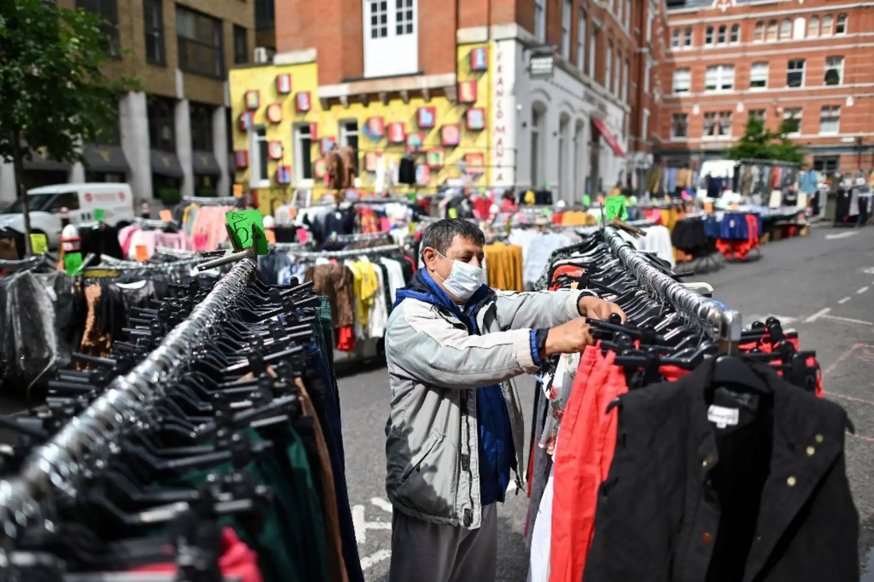 Un vendedor de puestos que usa equipo de protección personal, incluida una máscara facial como medida de precaución contra COVID-19, revisa su mercadería en su puesto de ropa en el mercado Petticoat Lane en Londres. Foto: AFP
