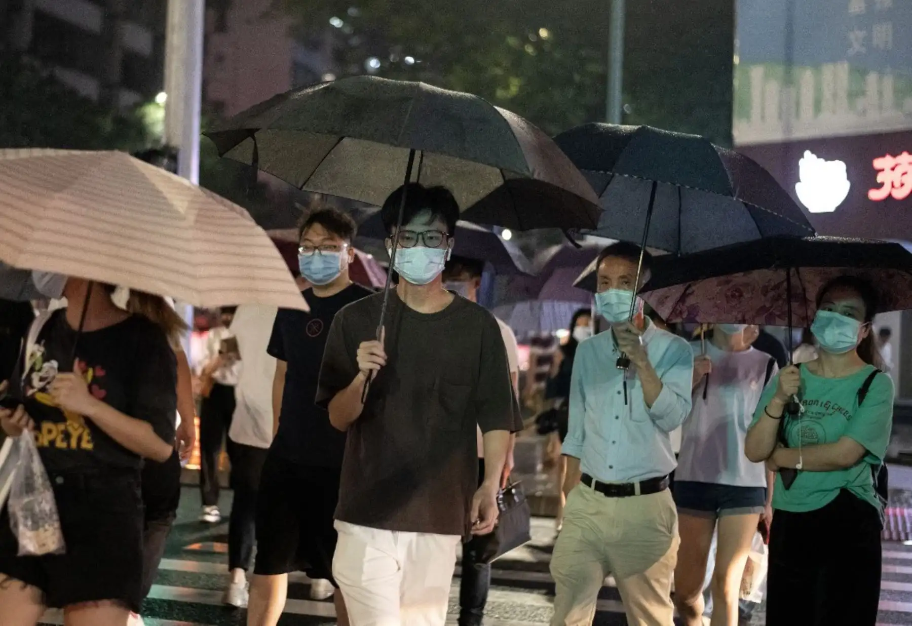 Las personas que usan mascarilla protectora caminan bajo sus paraguas mientras llueve en Shenzhen, en la provincia sureña china de Guangdong. Foto: AFP