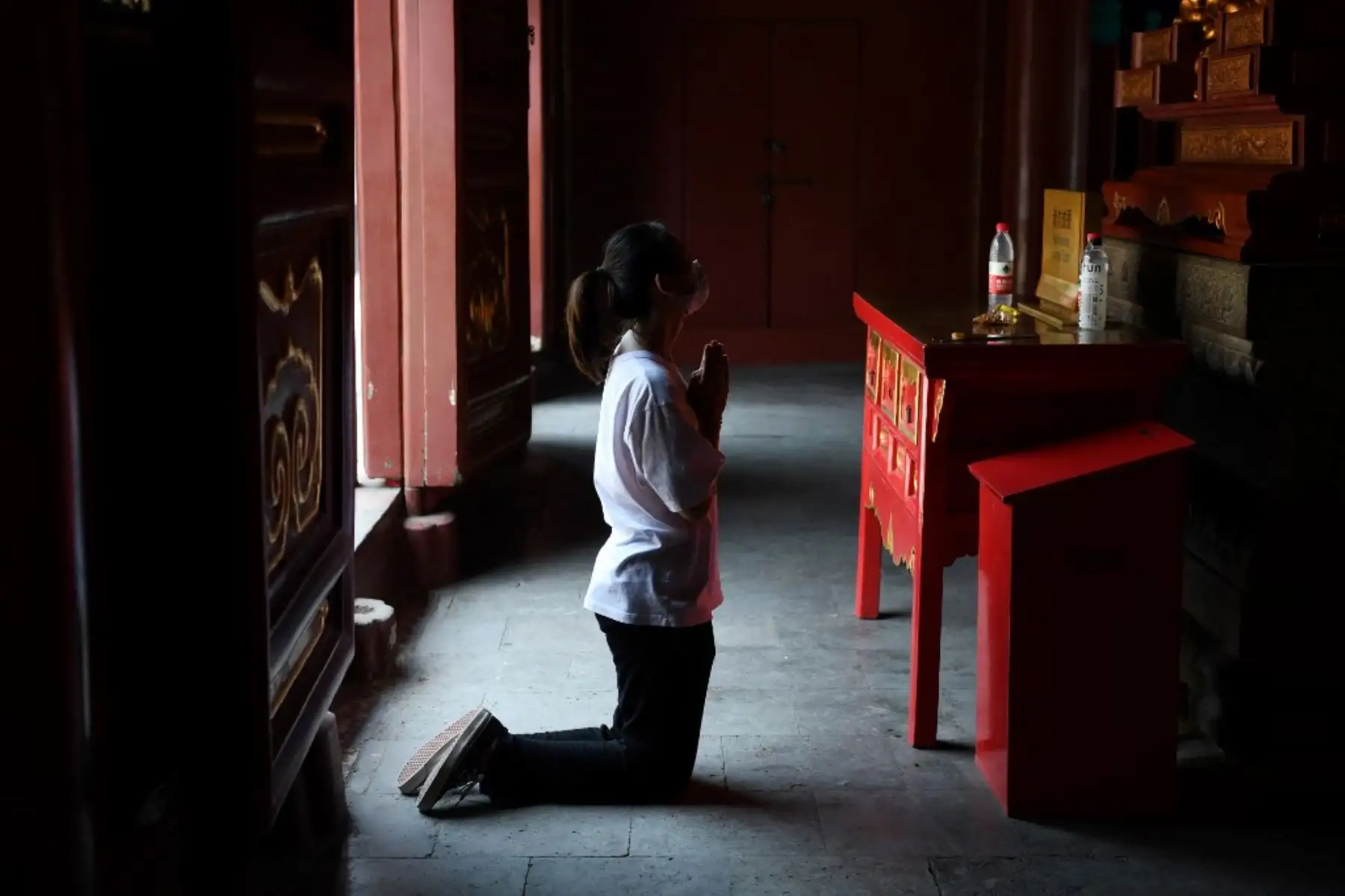 Una mujer que llevaba una máscara reza en el Templo Lama en Beijing. Foto: AFP