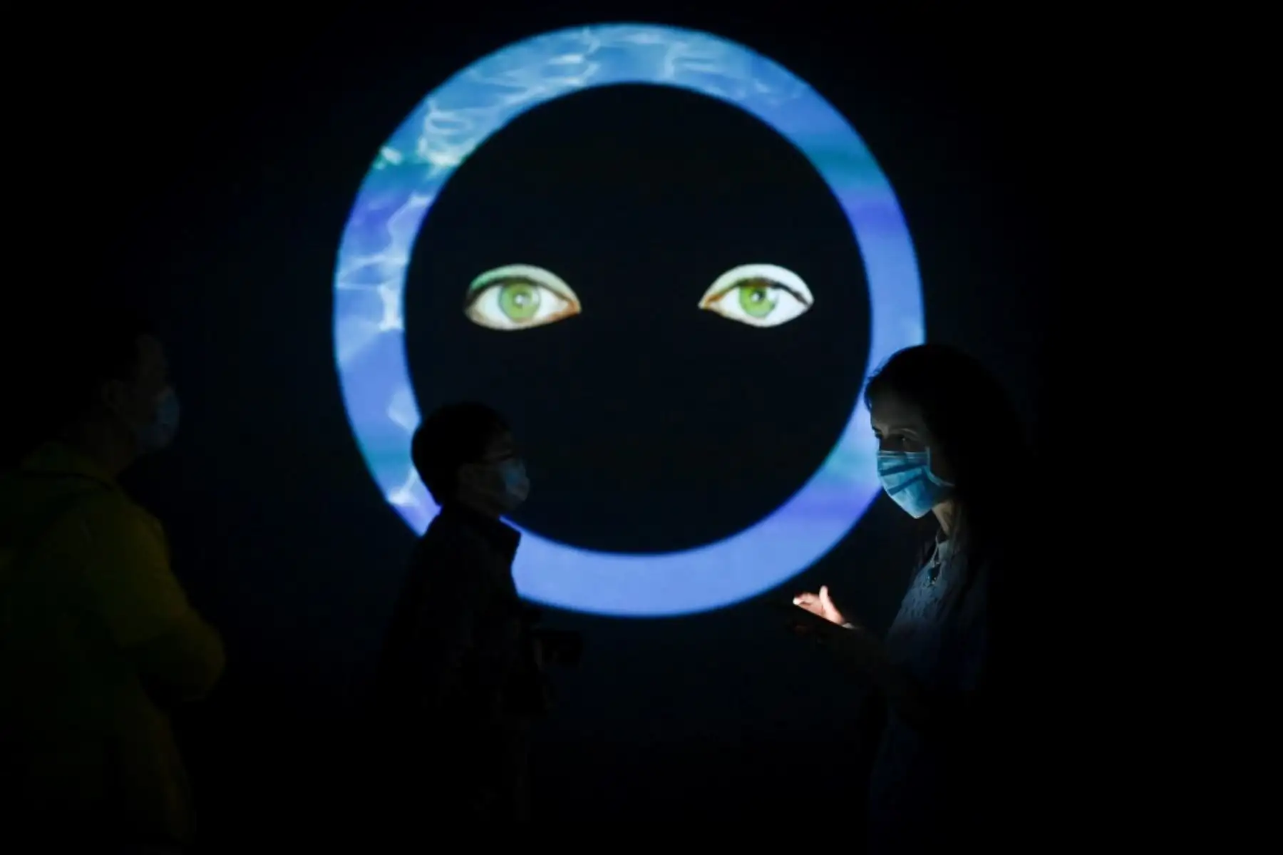 Una mujer que usa una máscara facial en medio de las preocupaciones por el coronavirus COVID-19 usa su teléfono móvil mientras visita la instalación de video "Whispering Pines" de Shana Moulton. Foto: AFP