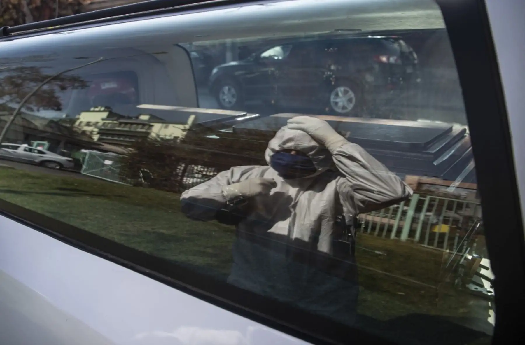 Un empleado de una casa funeraria se refleja en la ventanilla de un coche fúnebre mientras arregla su equipo de seguridad mientras espera afuera de la morgue del hospital público de San José, en Santiago. Foto: AFP